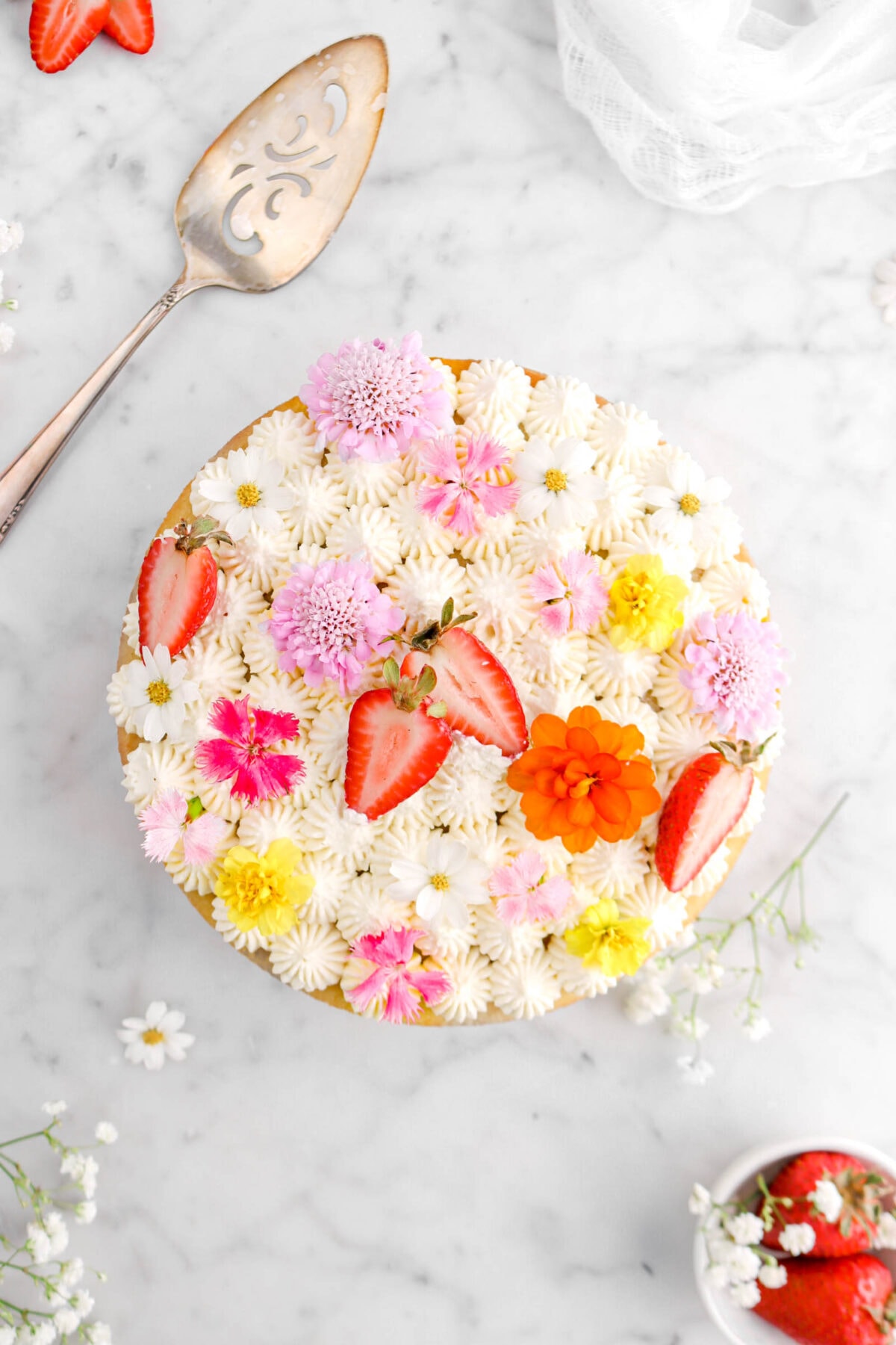 overhead shot of cake with piped frosting on top, fresh flowers, and strawberries