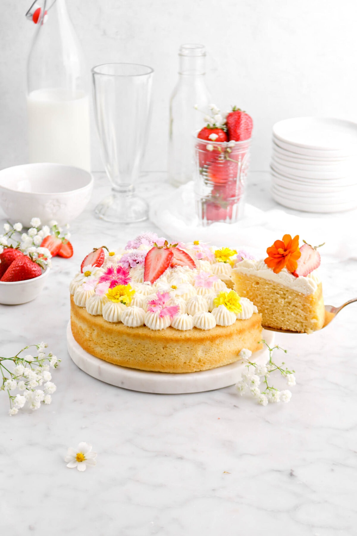 chamomile cake with slice being held by cake knife beside, with frosting on top, flowers, and strawberry halves