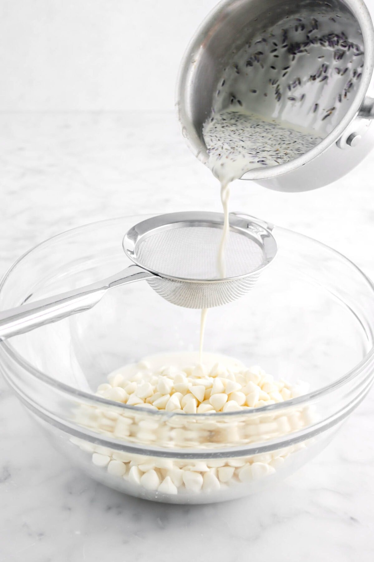 cream and lavender mixture being poured through a sieve into a bowl of white chocolate