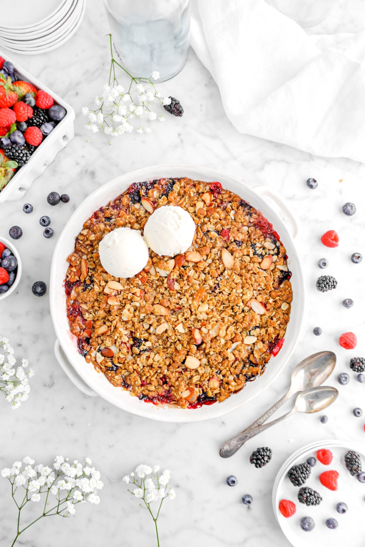 overhead shot of mixed berry crisp with berries scattered around, two spoons, and flowers