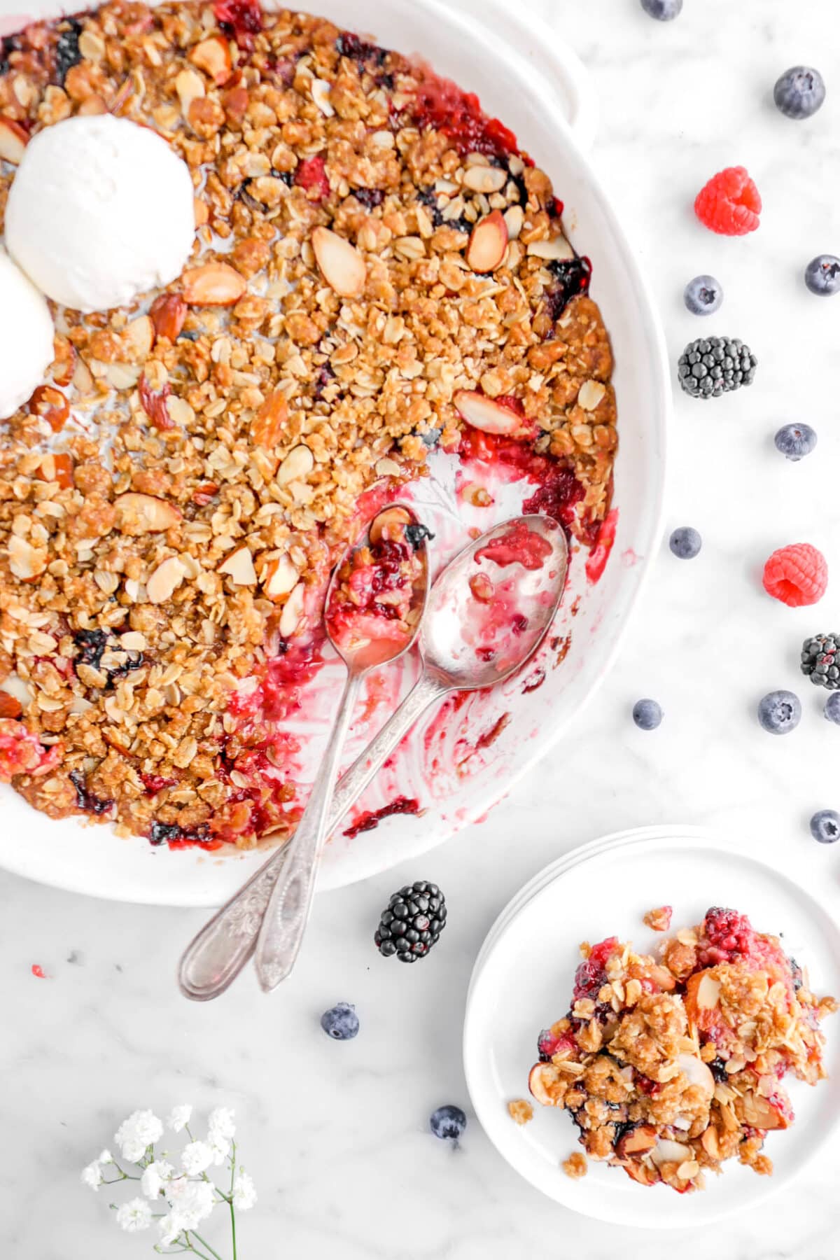 close up flat lay of two spoons in mixed berry crisp with plate beside