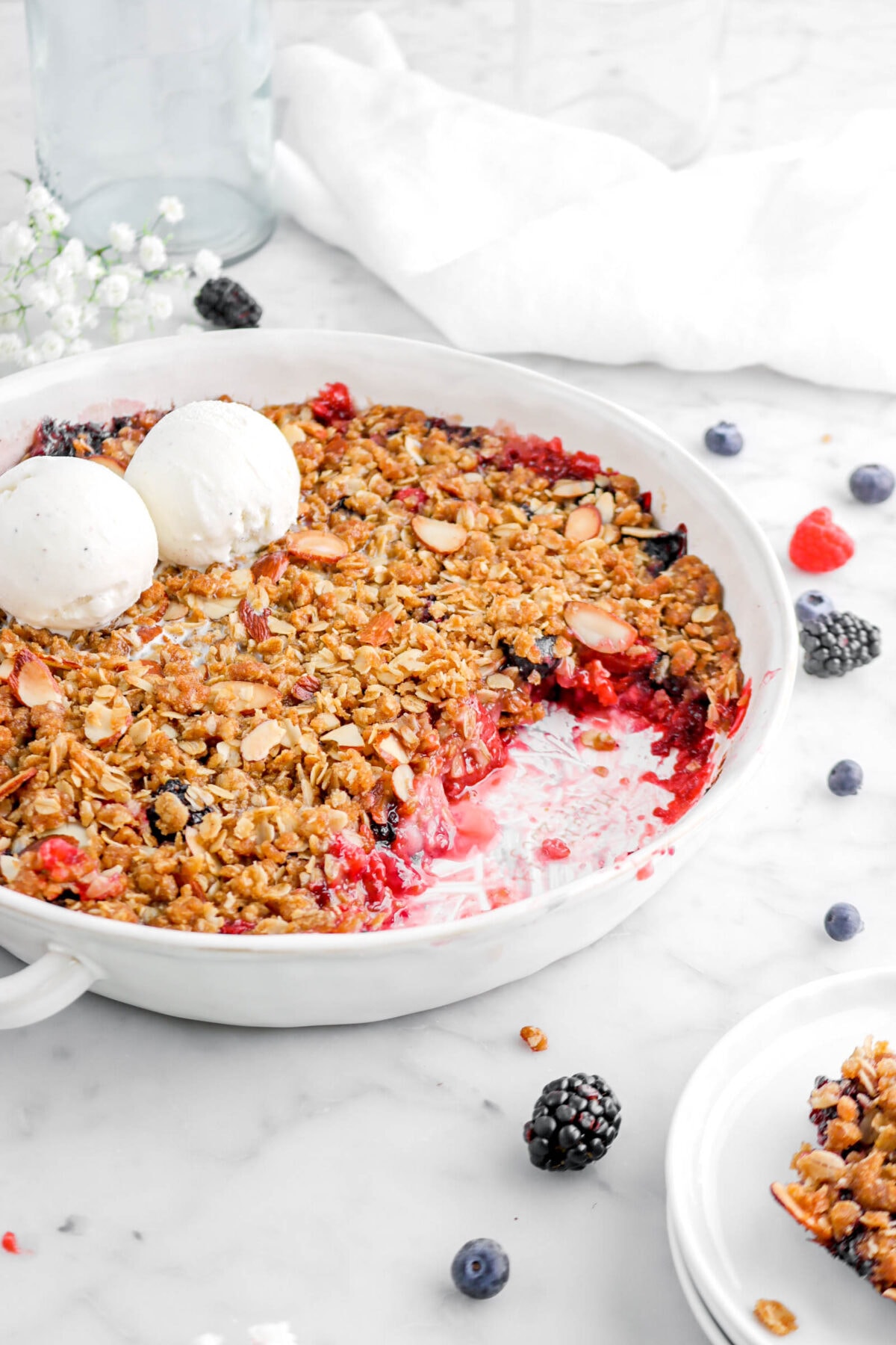 angled close up of mixed berry crisp with two scoops of ice cream on top and white napkin behind