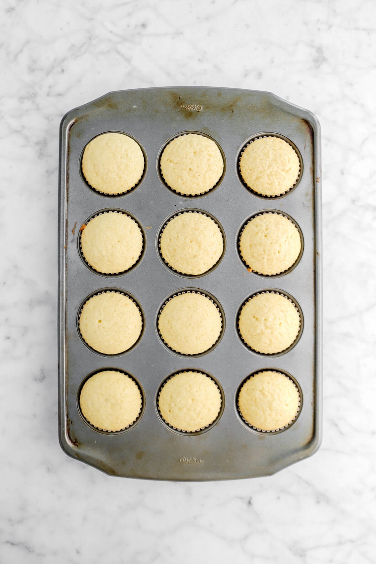 twelve baked vanilla cupcakes in cupcake pan