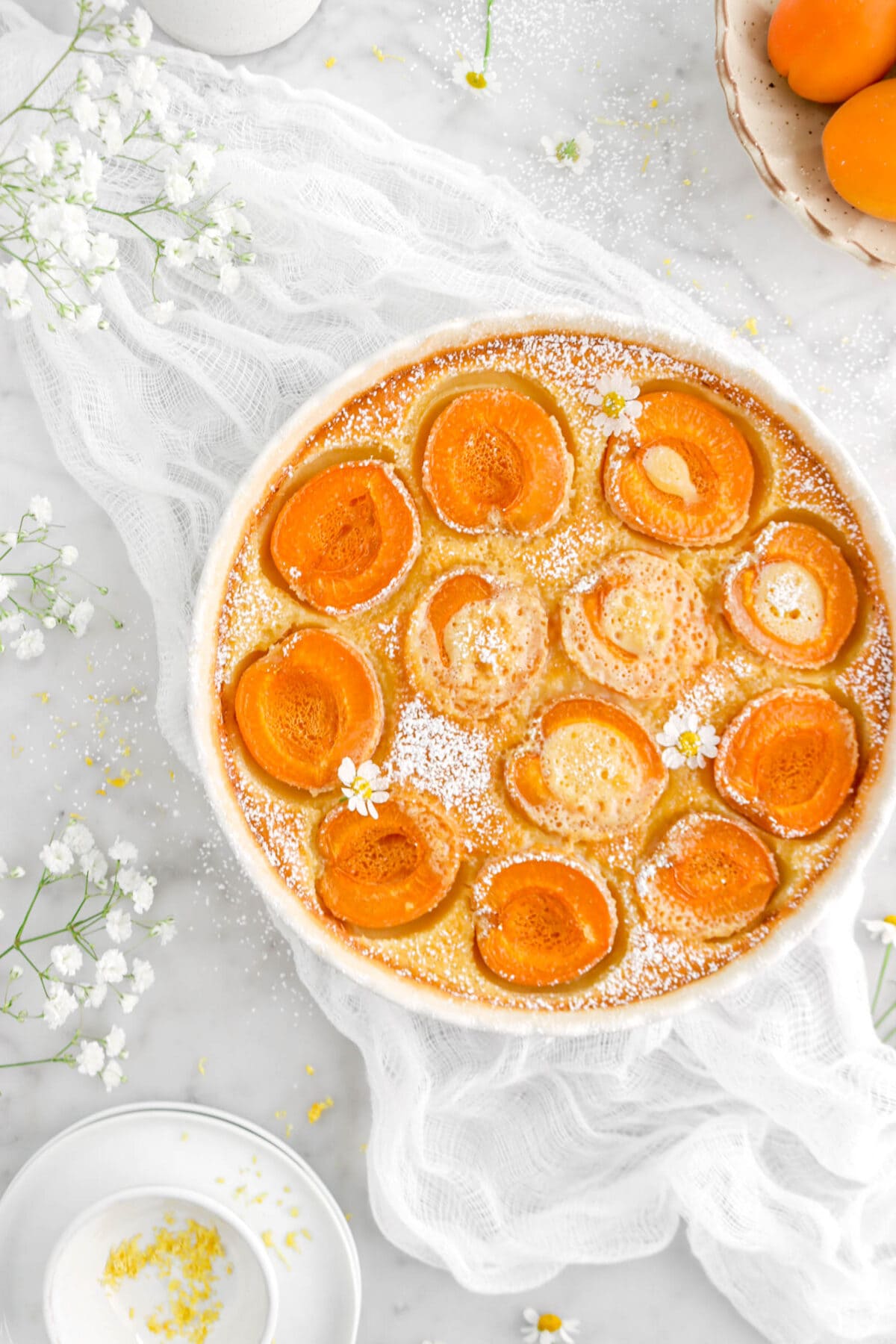flat lay of apricot clafoutis on white cheese cloth with flowers
