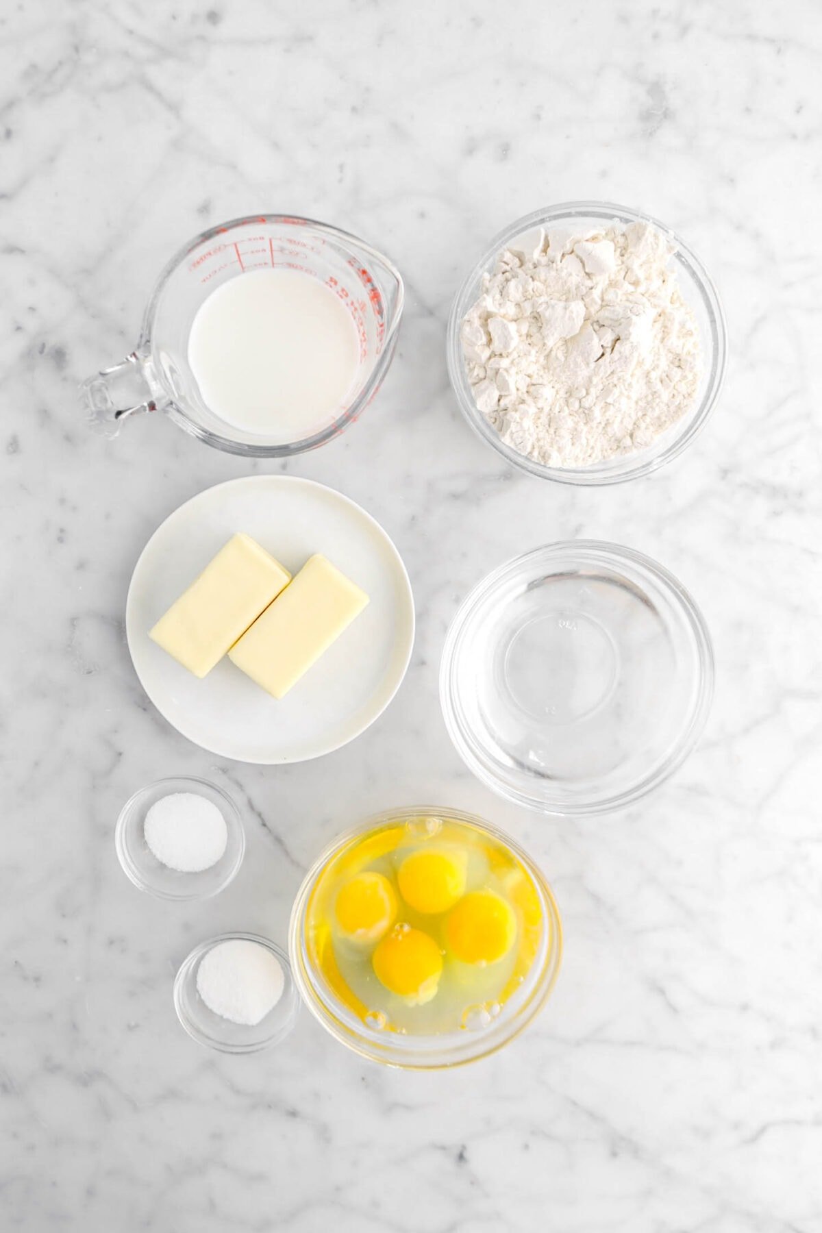 milk, flour, butter, water, salt, sugar, and eggs on marble surface