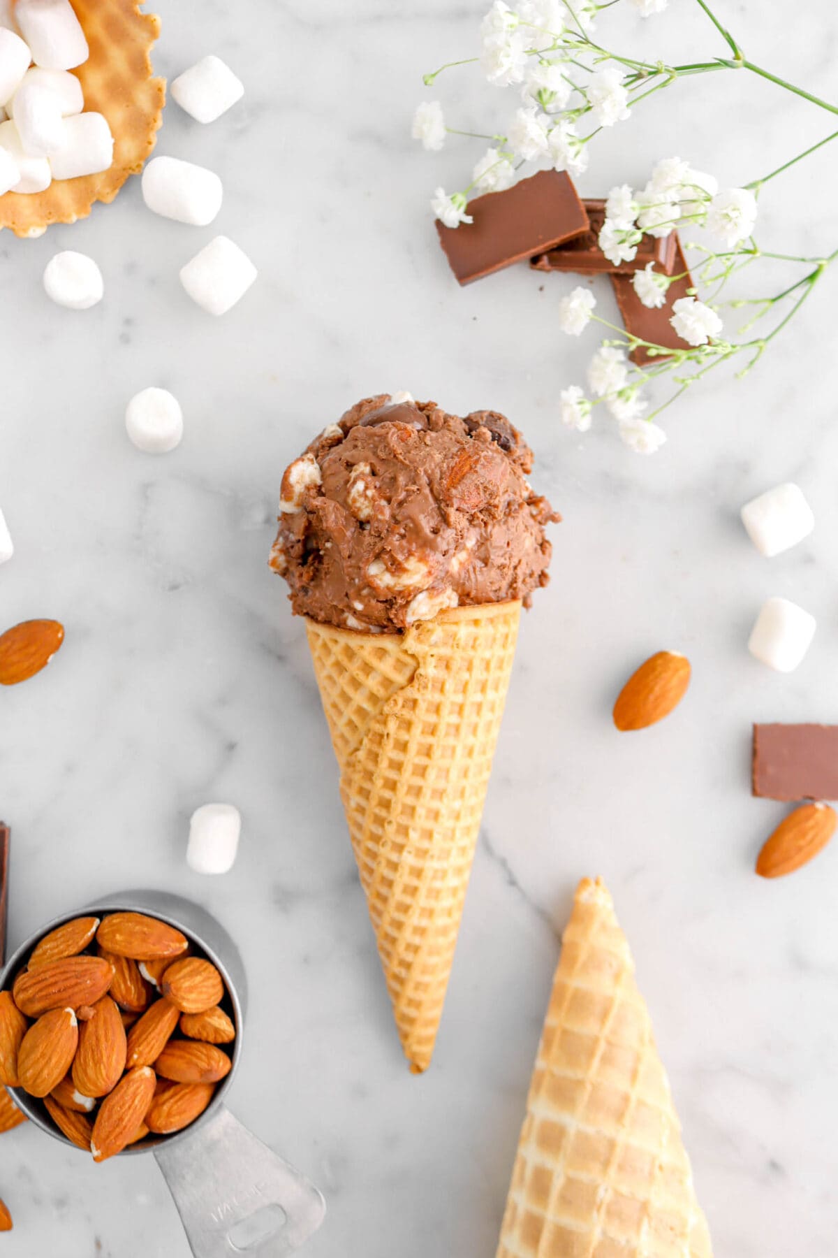 flat lay of rocky road ice cream scoop on marble surface with mini marshmallows, almonds, and chocolate pieces