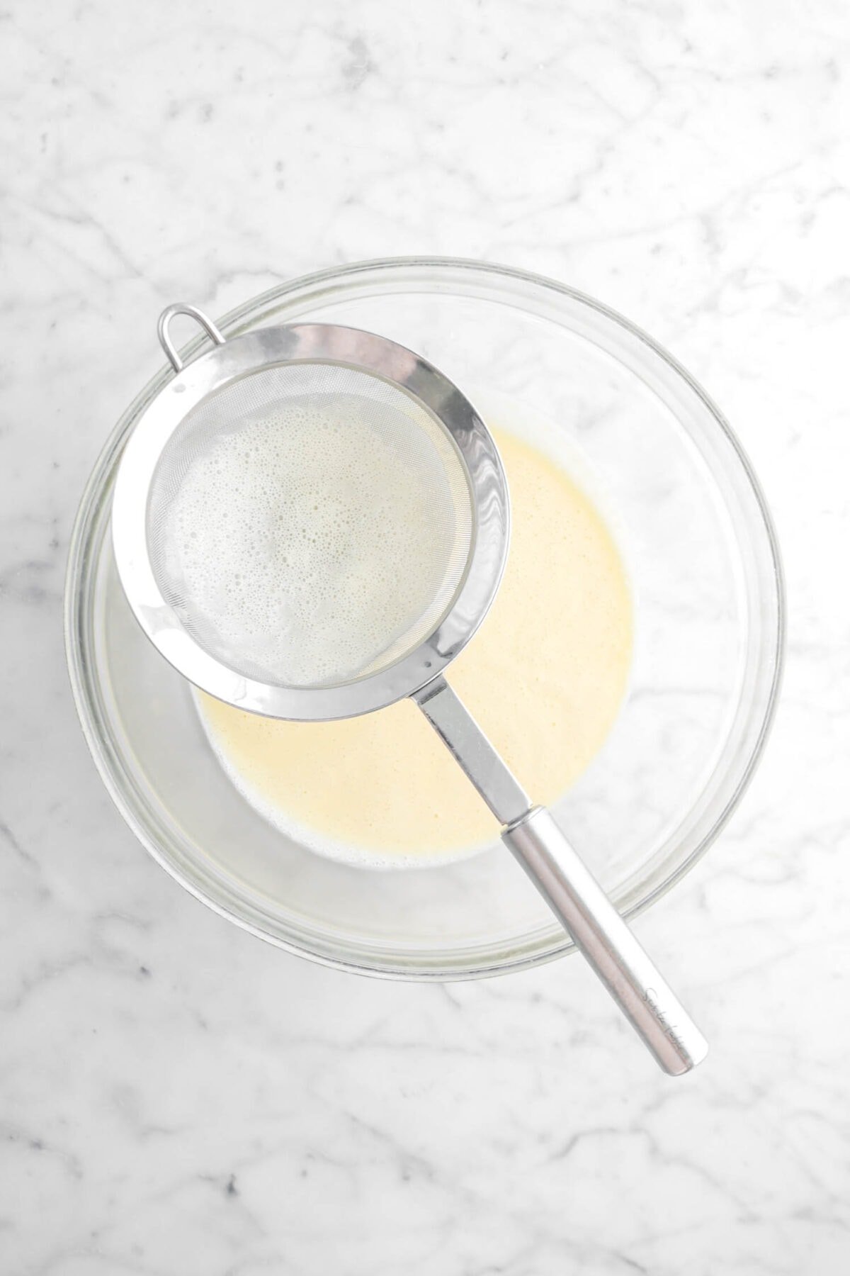 sieve sitting on top of large bowl with custard in bowl below