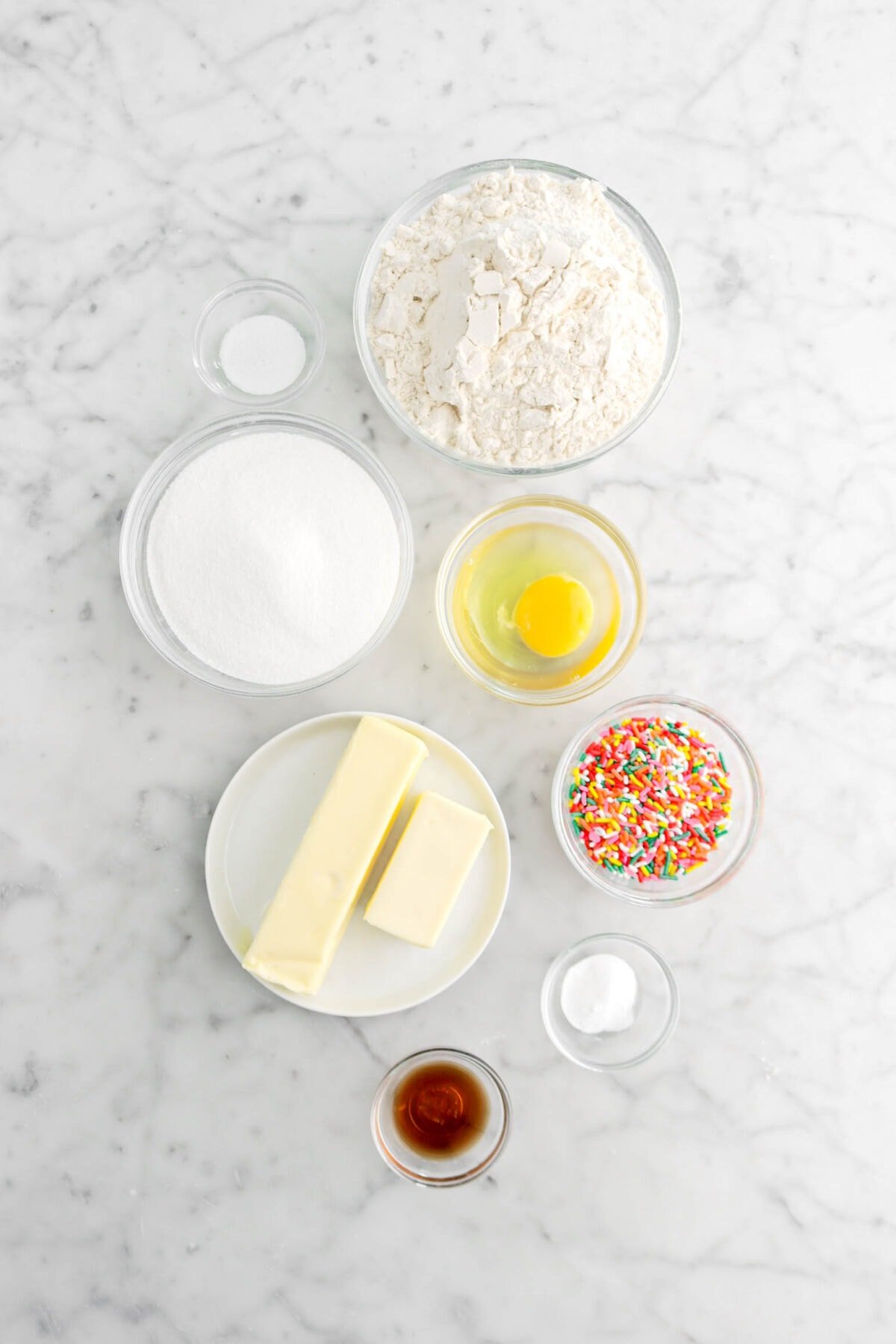 salt, flour, sugar, egg, sprinkles, butter, baking soda, and vanilla on marble surface