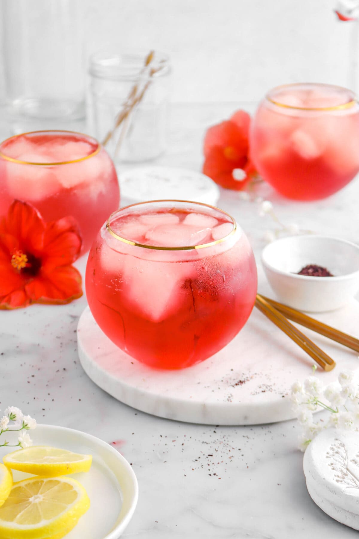 angled close up of cocktail on marble surface with two glasses and two hibiscus flowers behind