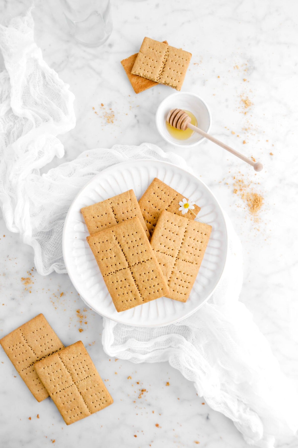 overhead shot of four graham crackers on a plate with two more beside and a bowl of honey