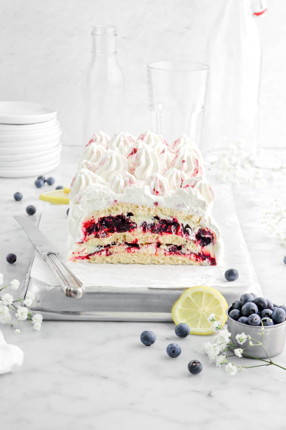 icebox cake on upside down sheet pan with layers of cake, mousse, and jam with a knife beside and blueberries around