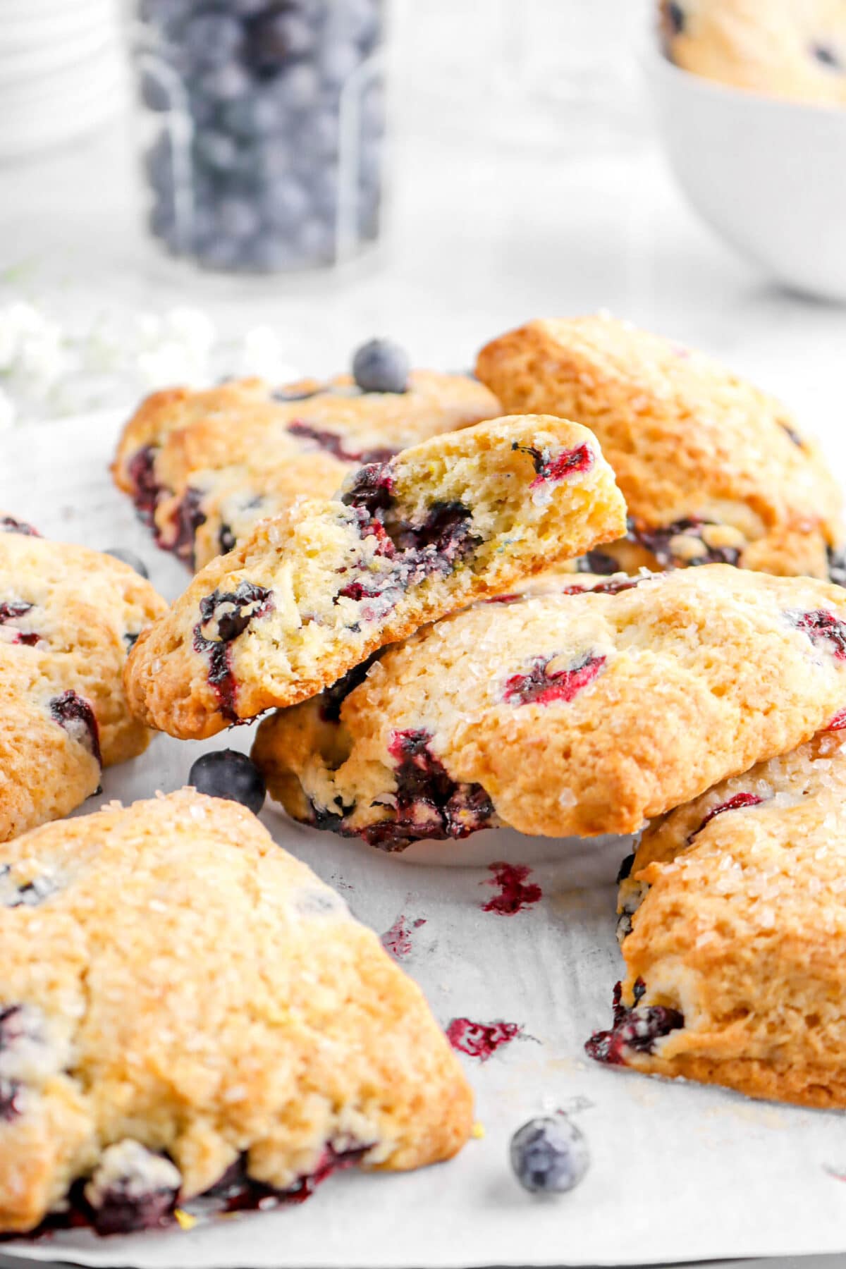 piled scones on parchment paper with jar of blueberries behind