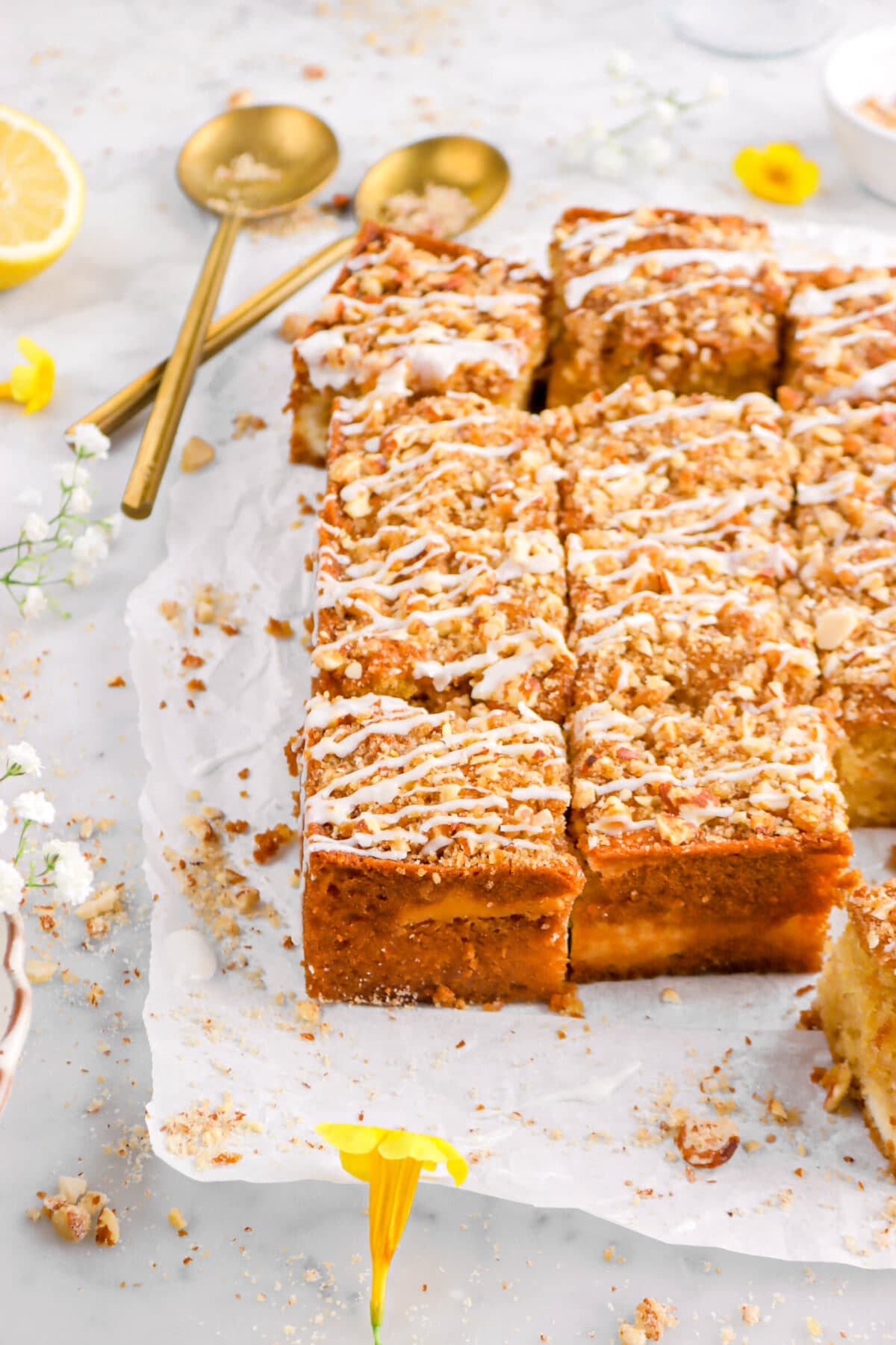 angled close up of sliced coffee cake on parchment paper with yellow flowers and two gold spoons behind