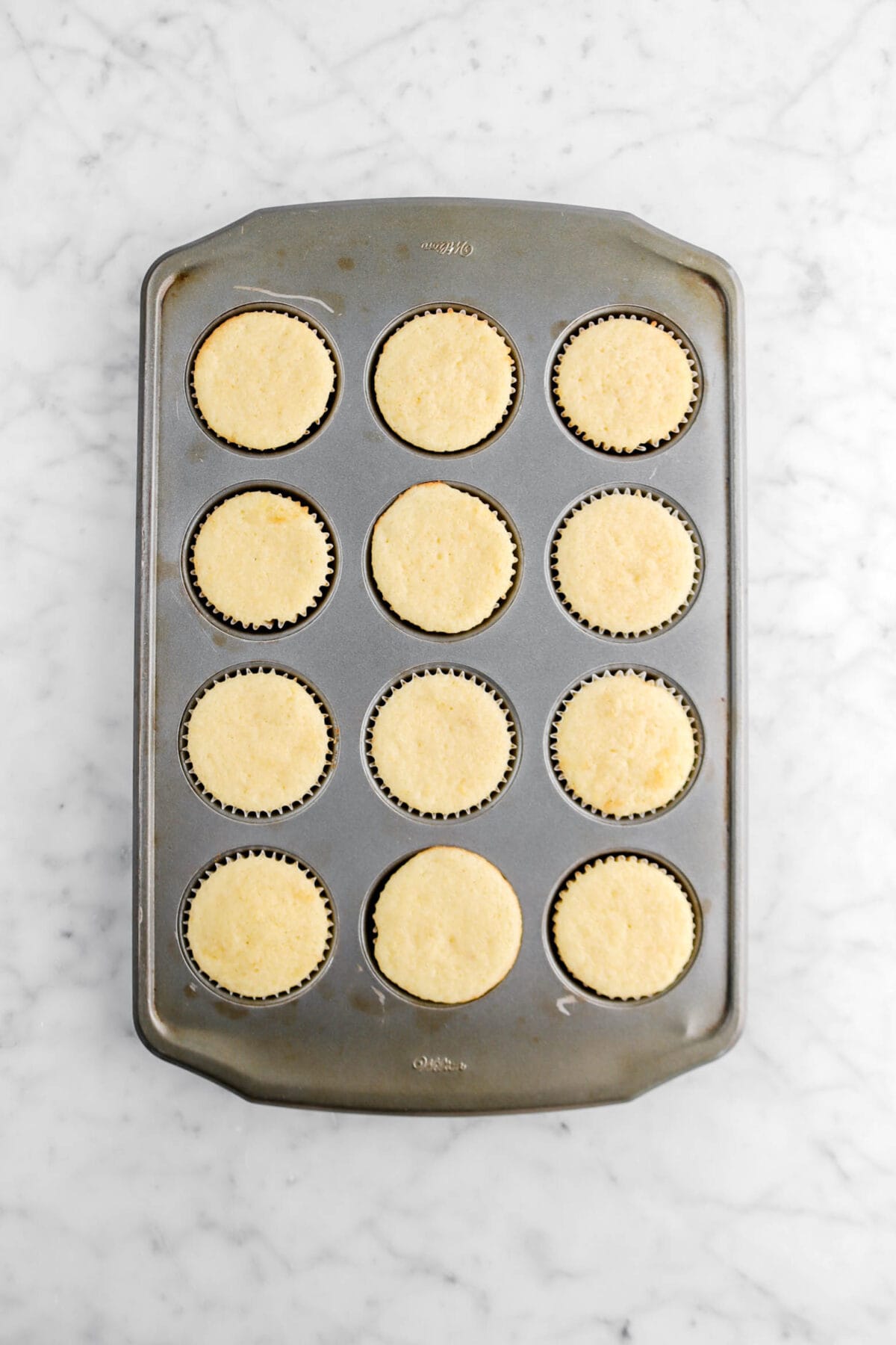 twelve baked lemon cupcakes on marble surface in cupcake pan