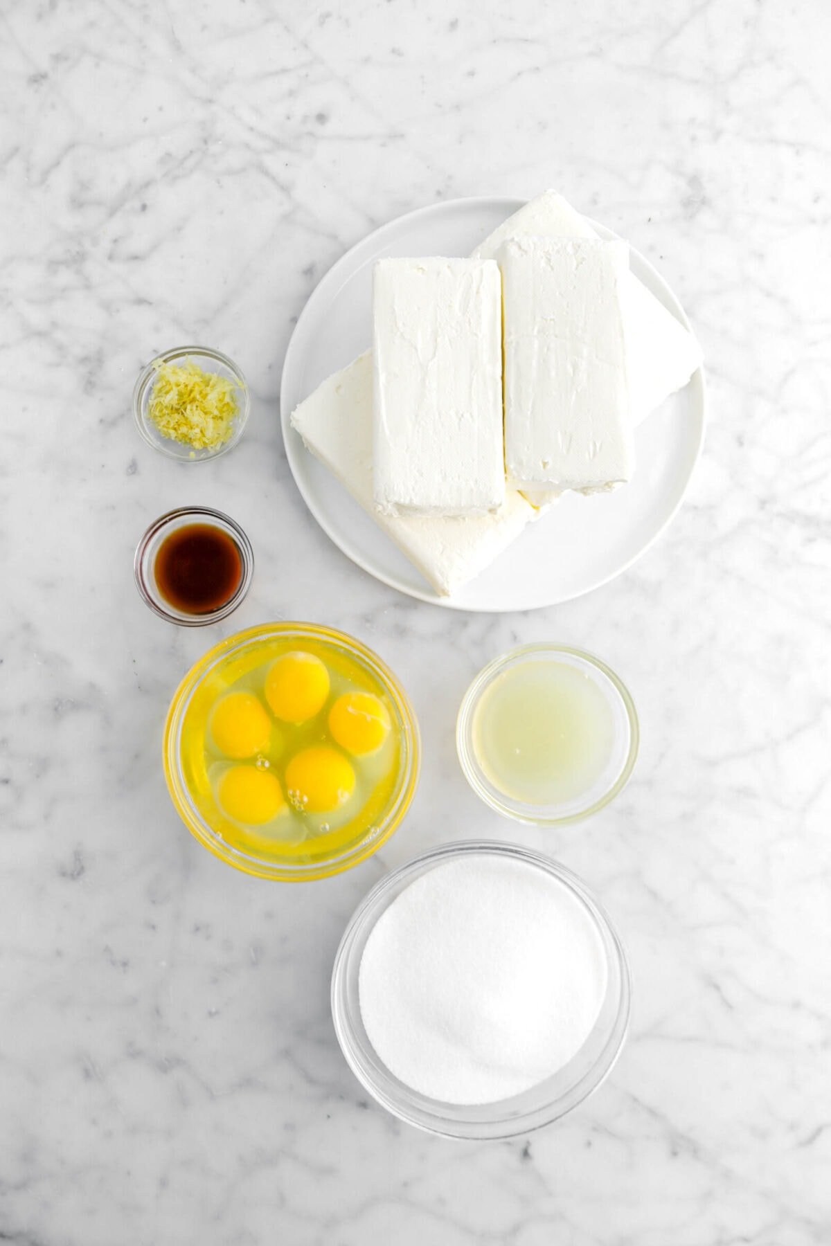 lemon zest, cream cheese blocks, vanilla, eggs, lemon juice, and sugar on marble surface