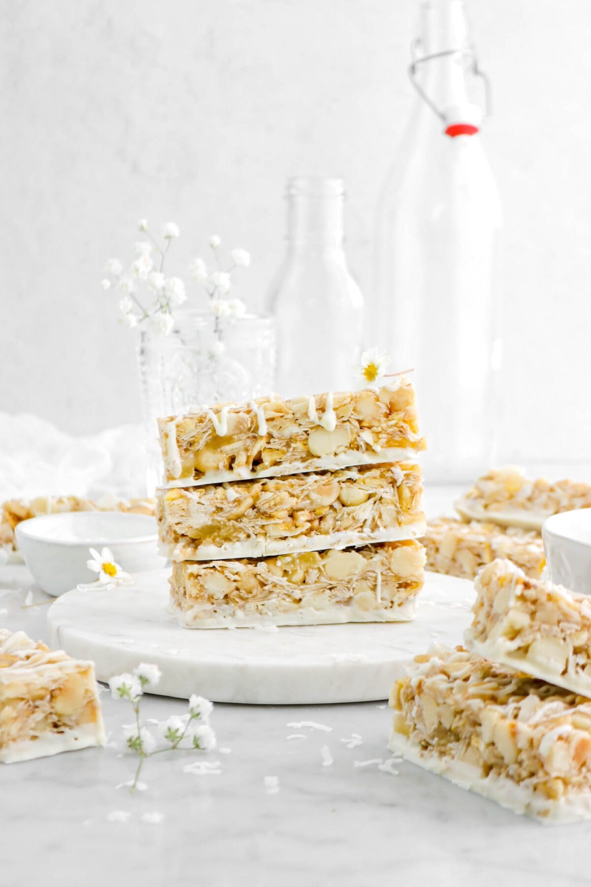 three stacked granola bars turned horizontally on marble surface with more granola bars around and a flower on top