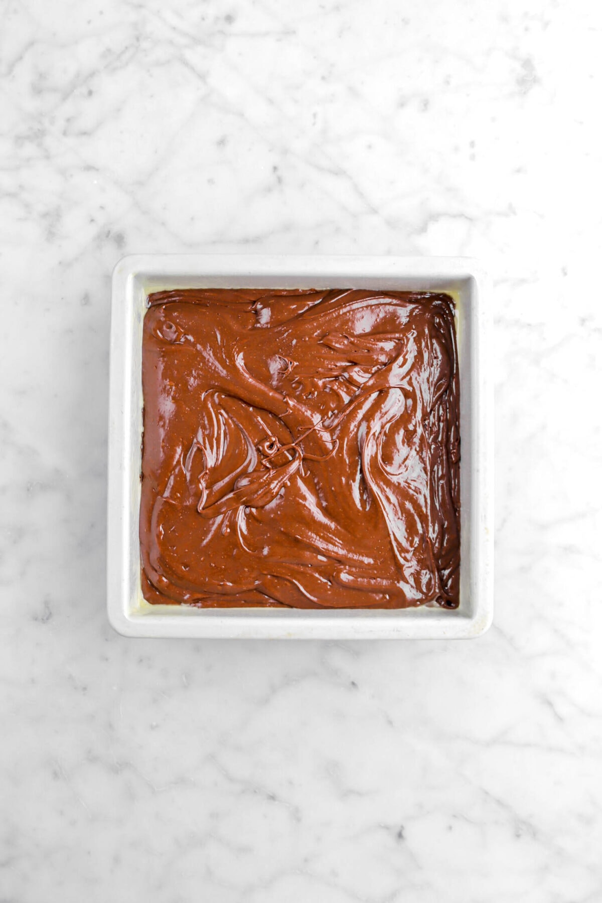 brownie batter in square pan on marble surface