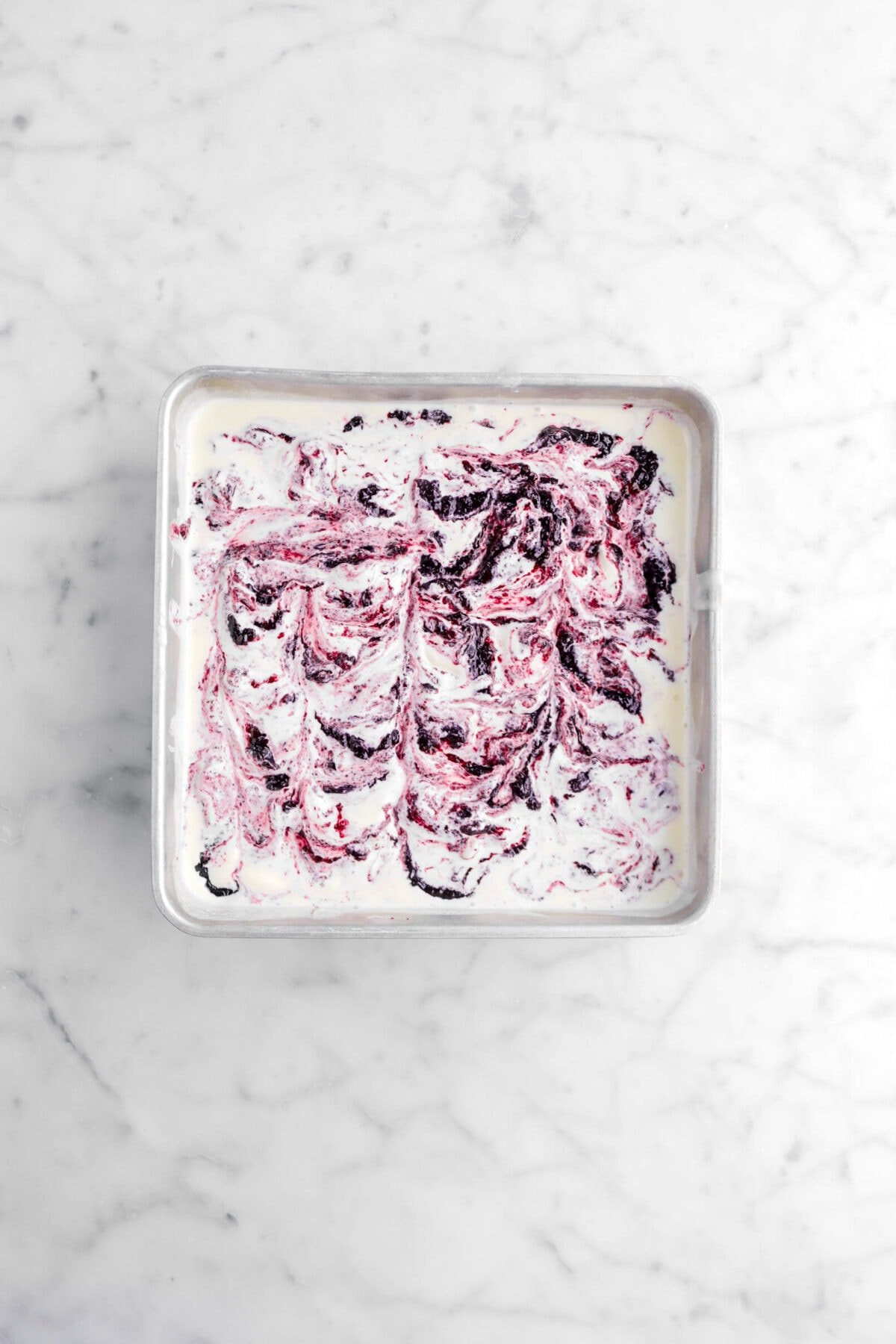 blueberry jam swirled into ice cream in square pan an on marble surface