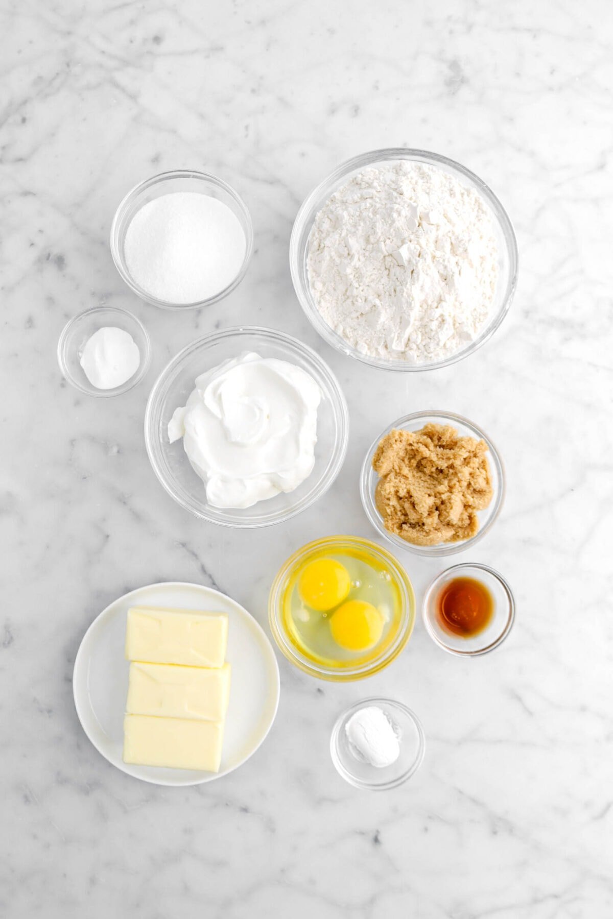 sugar, baking soda, sour cream, flour, brown sugar, eggs, butter, baking powder, and vanilla on marble surface