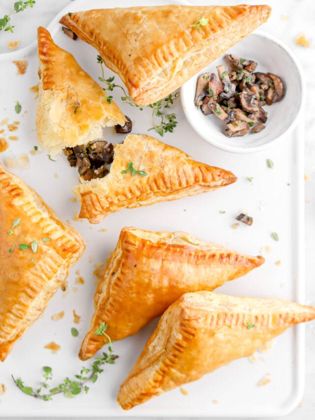 overhead shot of turnovers on white square with bowl of mushrooms and one turnover broken open