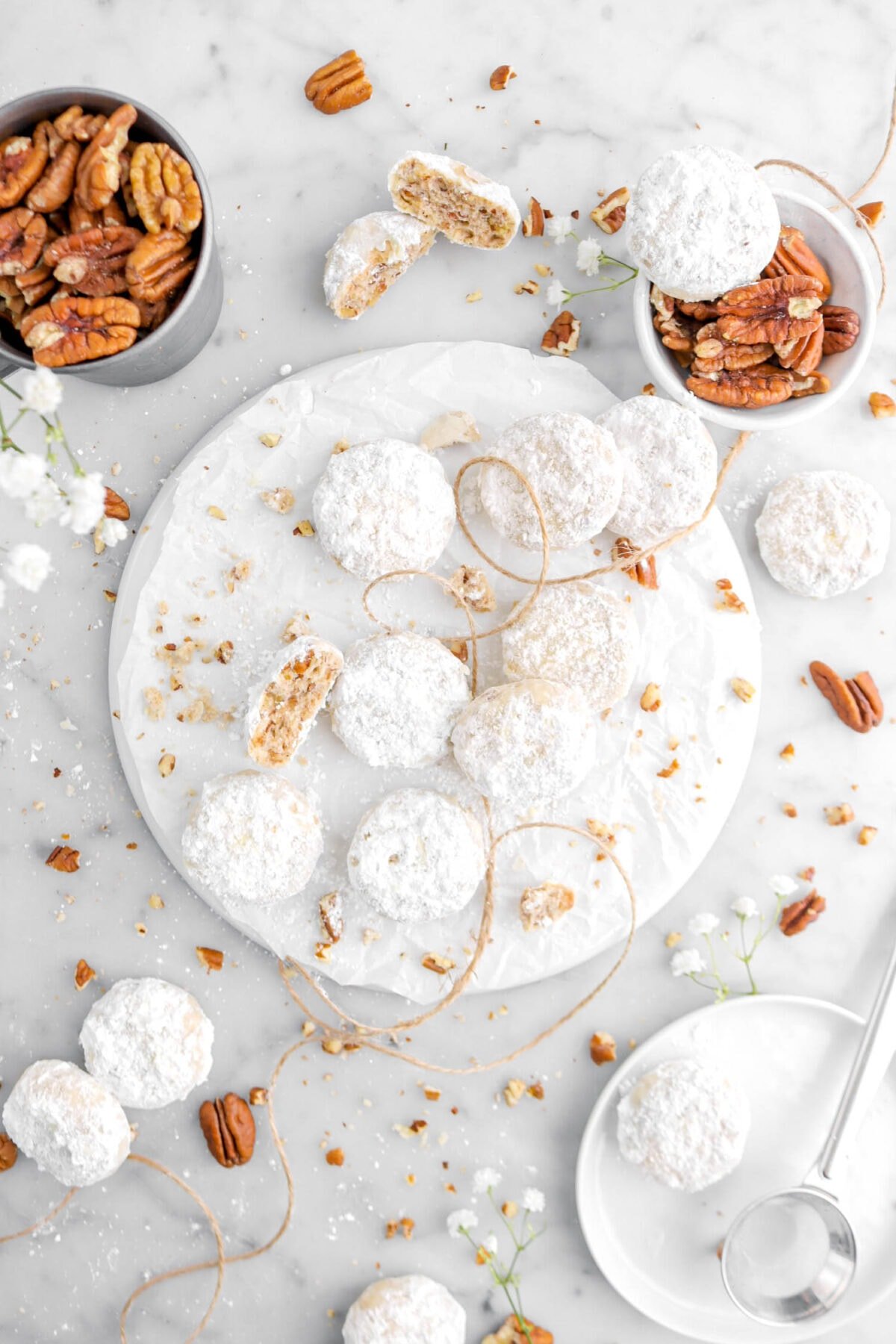 overhead shot of cookies on white plate with one broken in half, pecans and flowers around