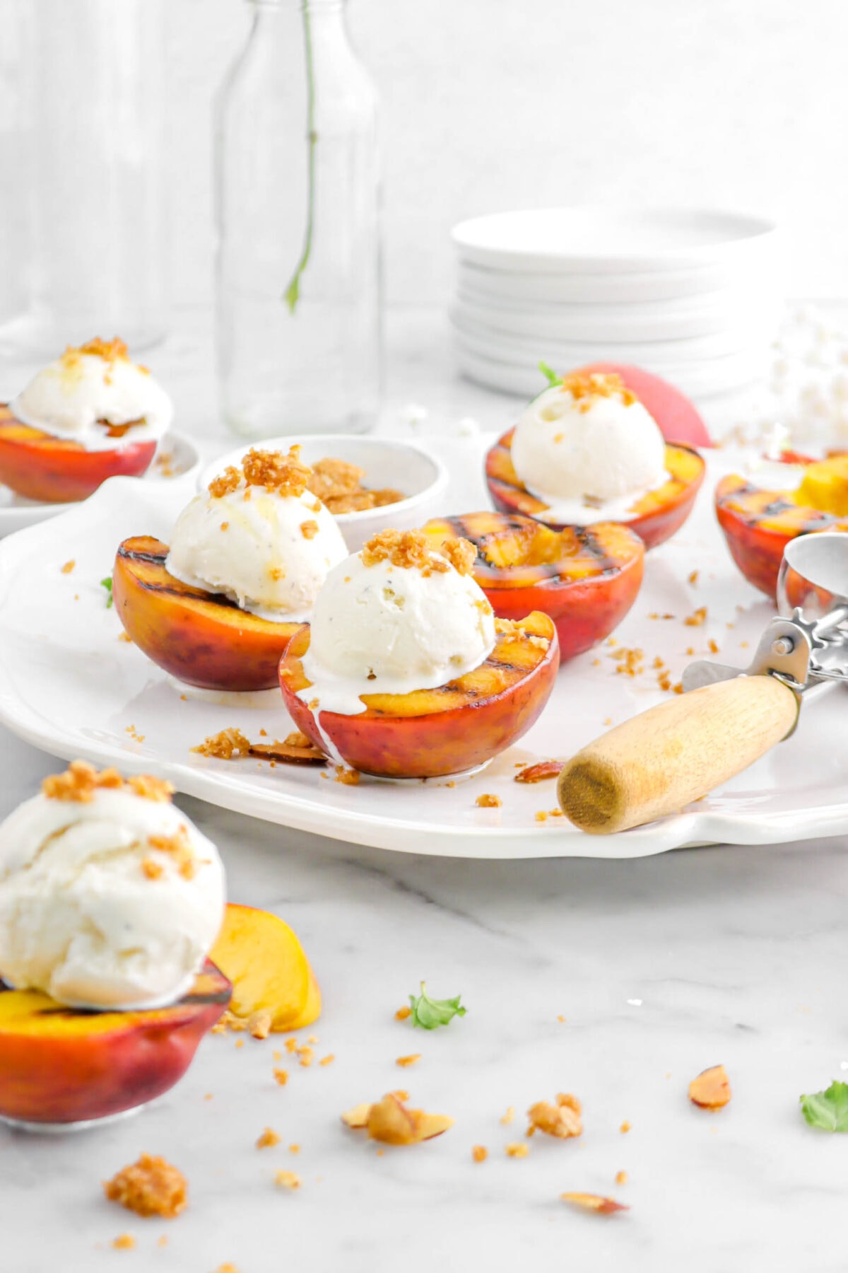 front shot of grilled peaches with ice cream on top on white platter