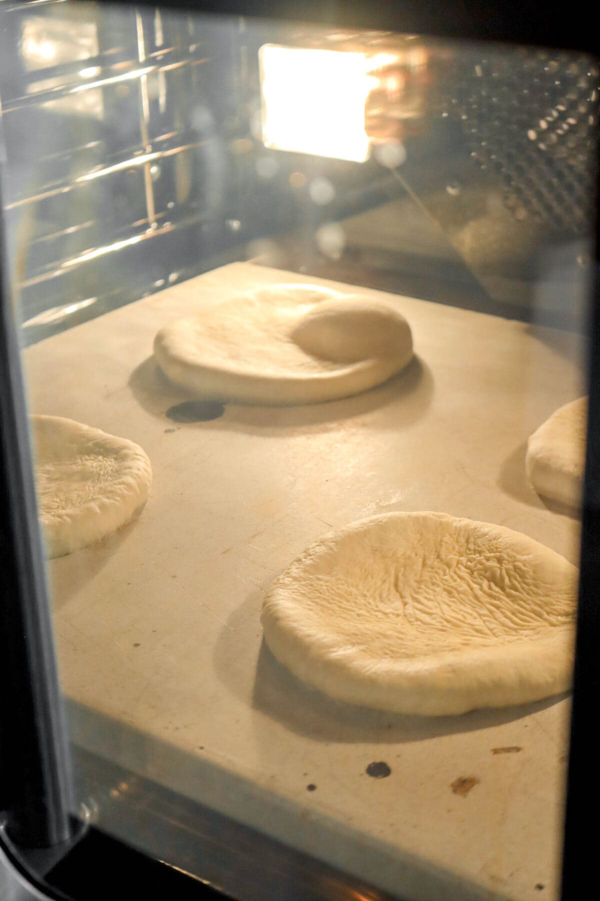 four flat and unbaked pitas in oven on stone