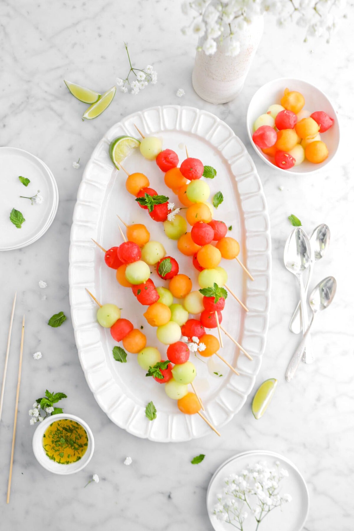 melon skewers on white platter with mint sprigs and white flowers
