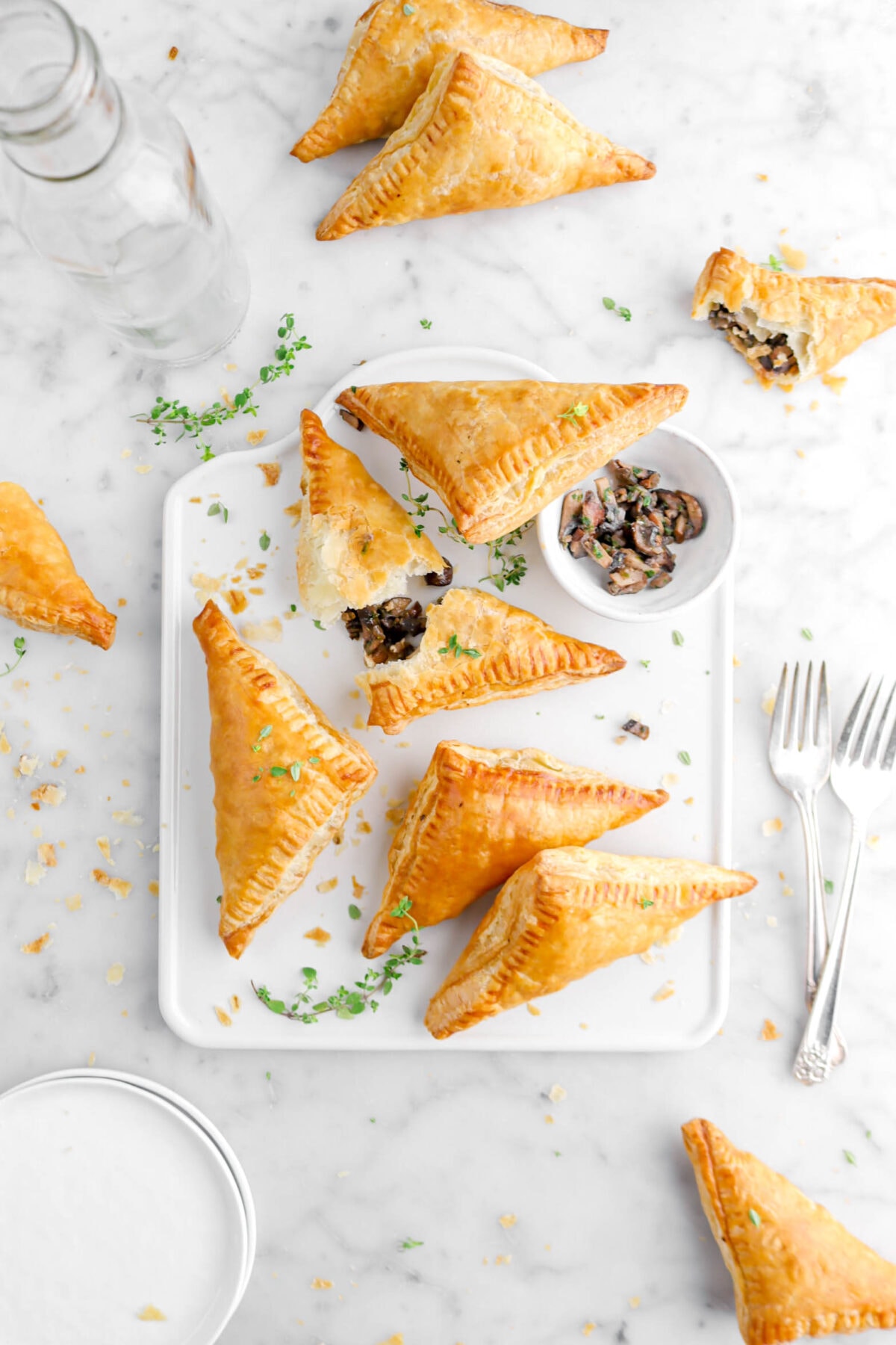 overhead shot of five turnovers on square serving tray, with one turnover broken open, a bowl of mushrooms, and thyme sprigs around