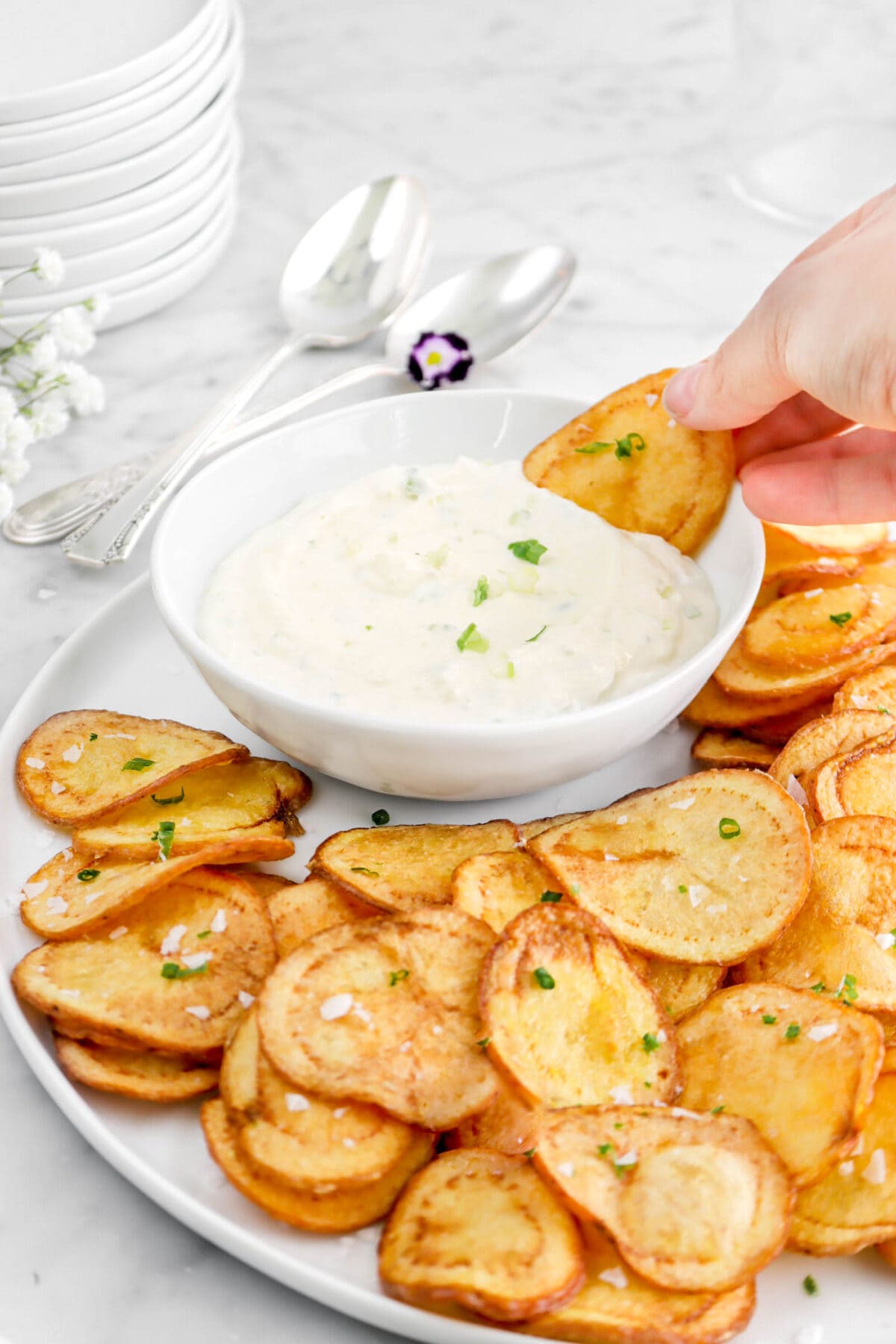 hand dipping chip into dip with more chips around on white plate