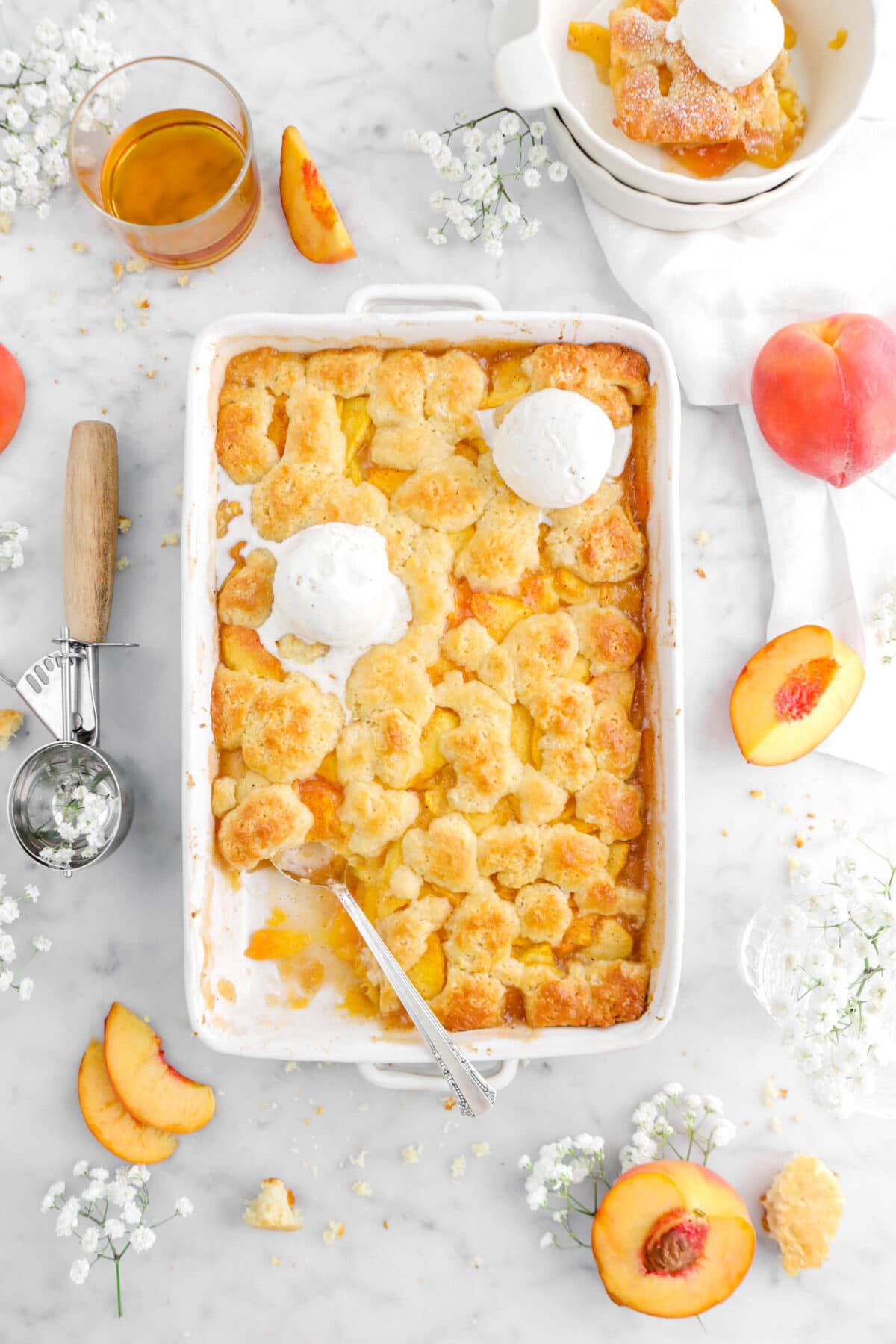 overhead shot of peach cobbler with spoon stuck inside, two scoops of ice cream on top, and peaches around