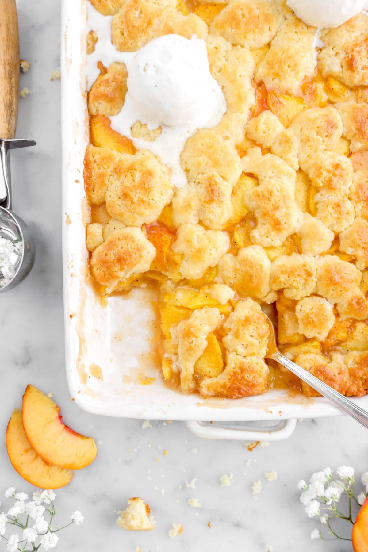 close up of peach cobbler with spoon under slice in white casserole
