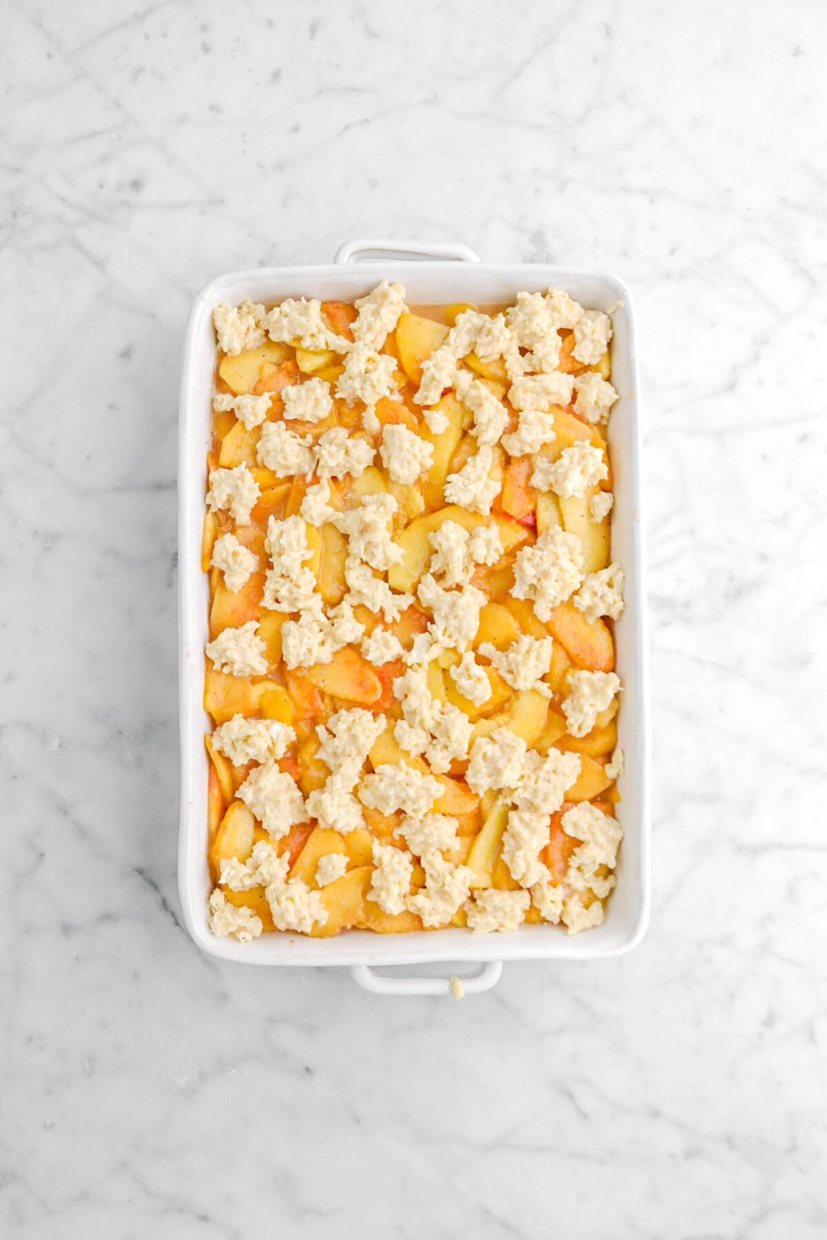 crumbled dough on top of peach filling in glass casserole