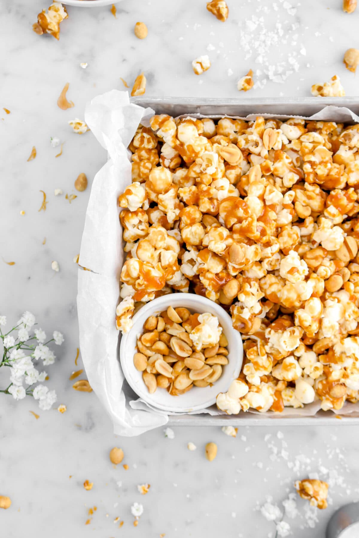 cropped close up of toffee popcorn with bowl of peanuts on marble surface