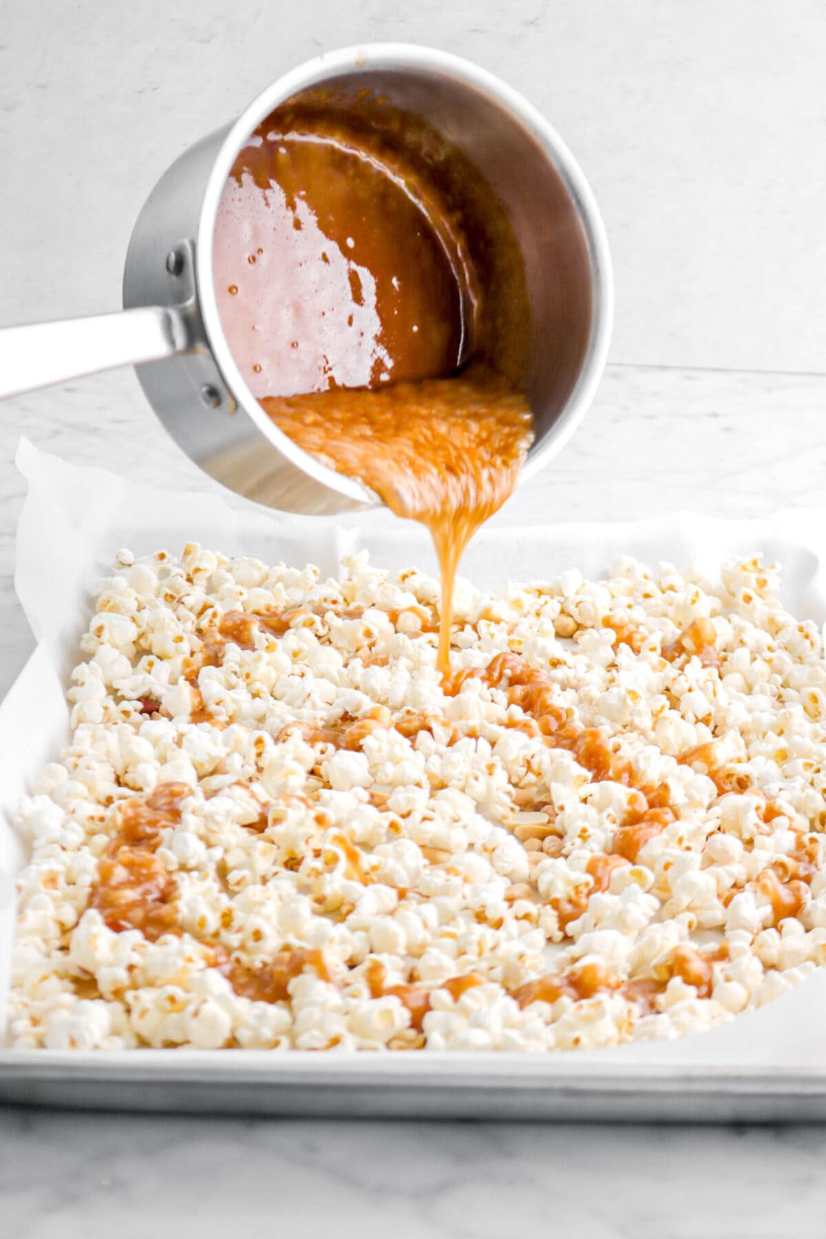 toffee being poured over popcorn in lined sheet pan