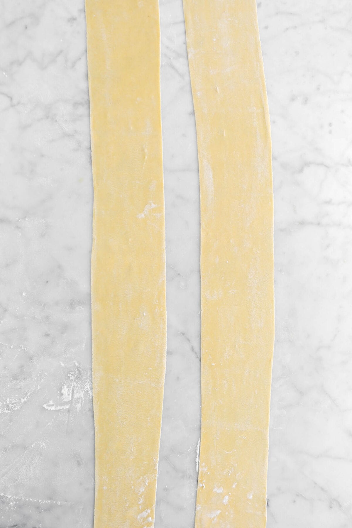 two sheets of pasta on marble surface.
