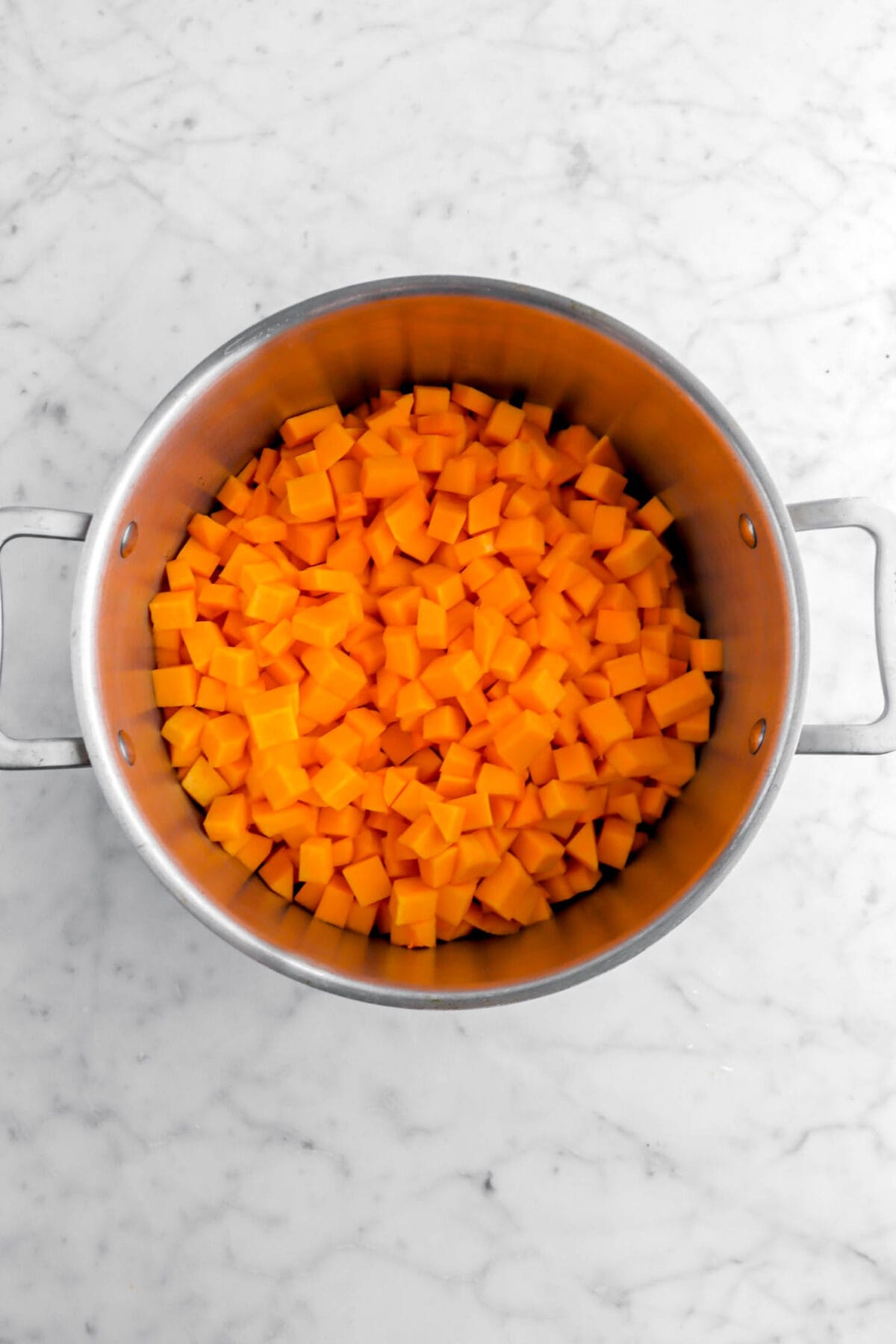chopped butternut squash in large pot on marble surface.