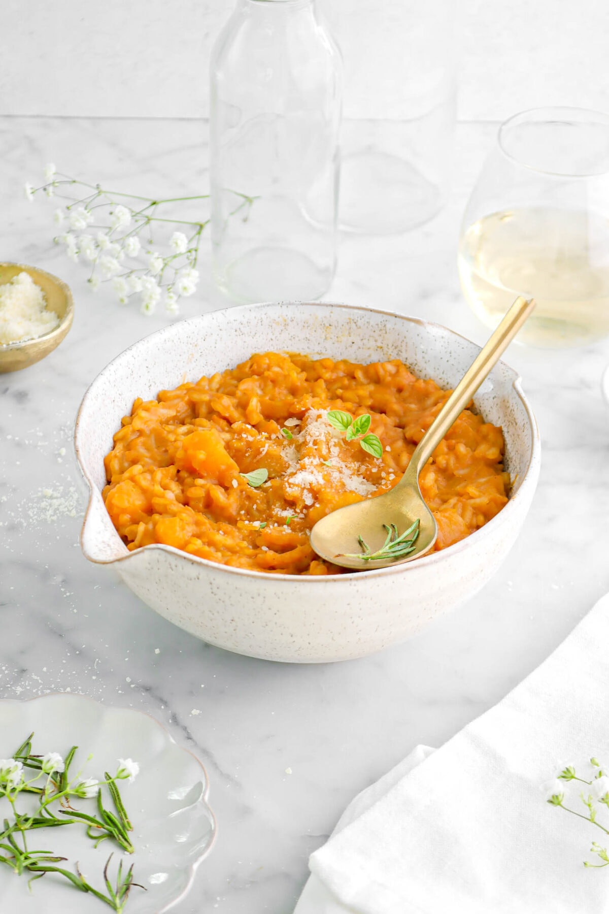 front shot of butternut squash risotto in large bowl with gold spoon on top, with glass of wine behind.