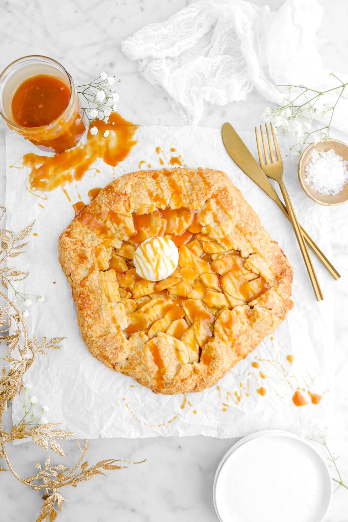 overhead shot of caramel apple galette with scoop of ice cream on top, gold garland beside, and gold fork and knife beside