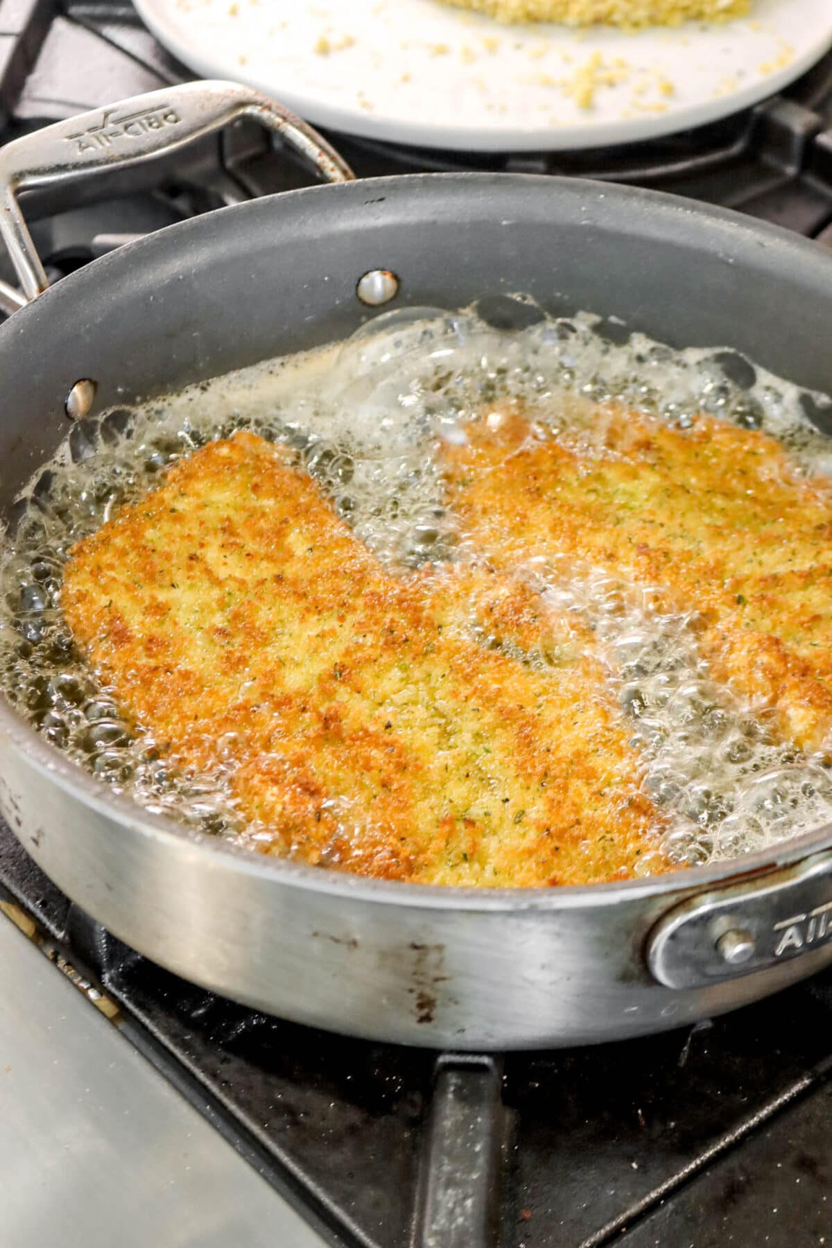 two browned breadcrumb coated chicken breasts in oil