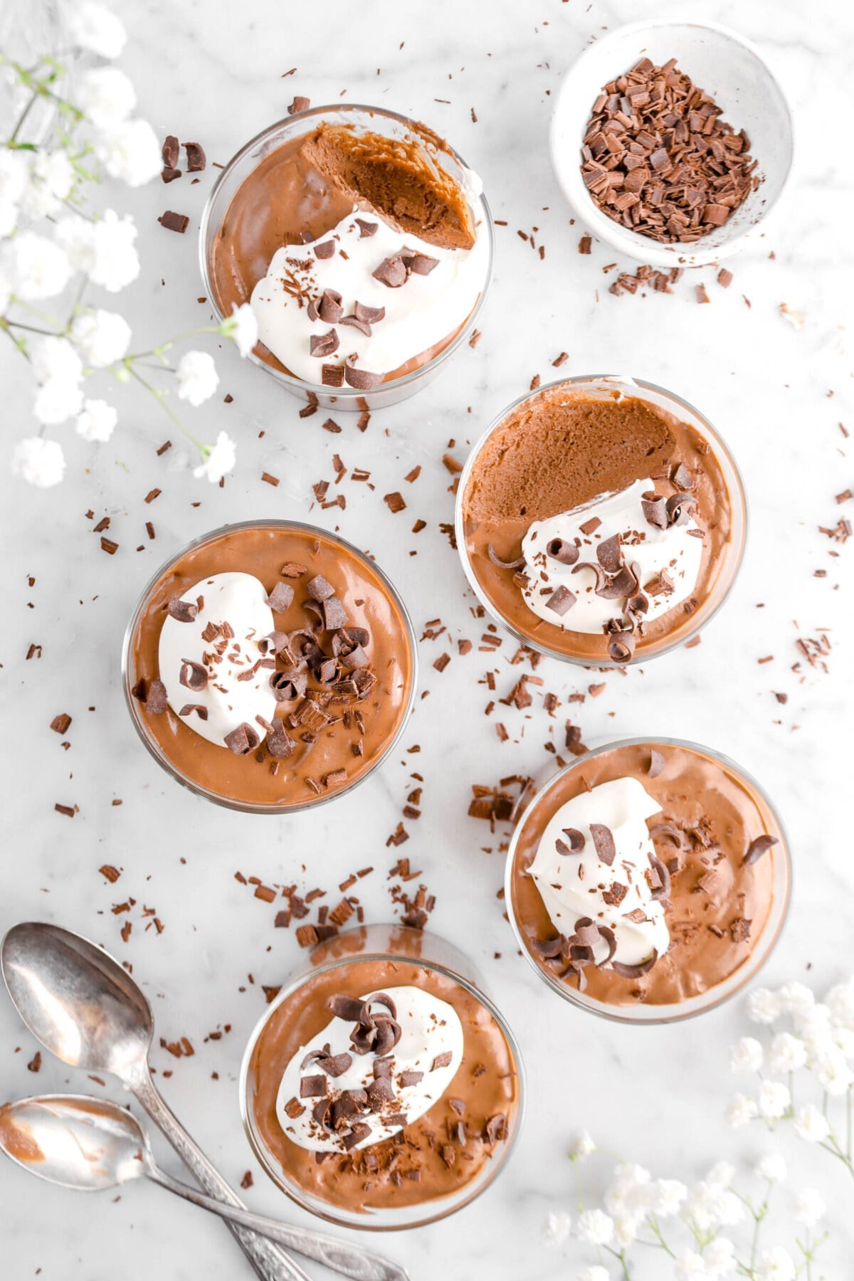 overhead shot of five glasses of chocolate mousse with spoonful missing from two glasses, with bowl of chocolate curls beside