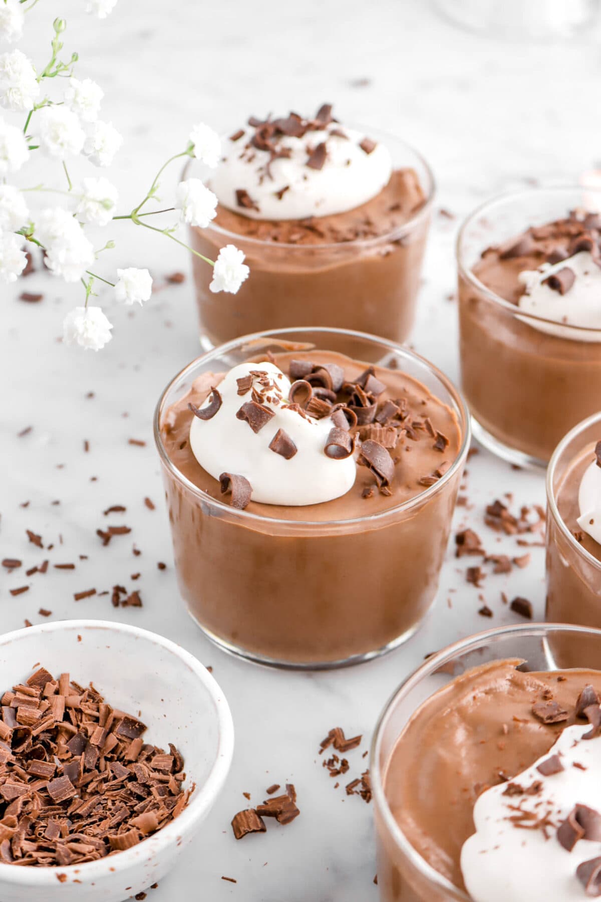 angled close up of glass of chocolate mousse with chocolate curls and white flowers
