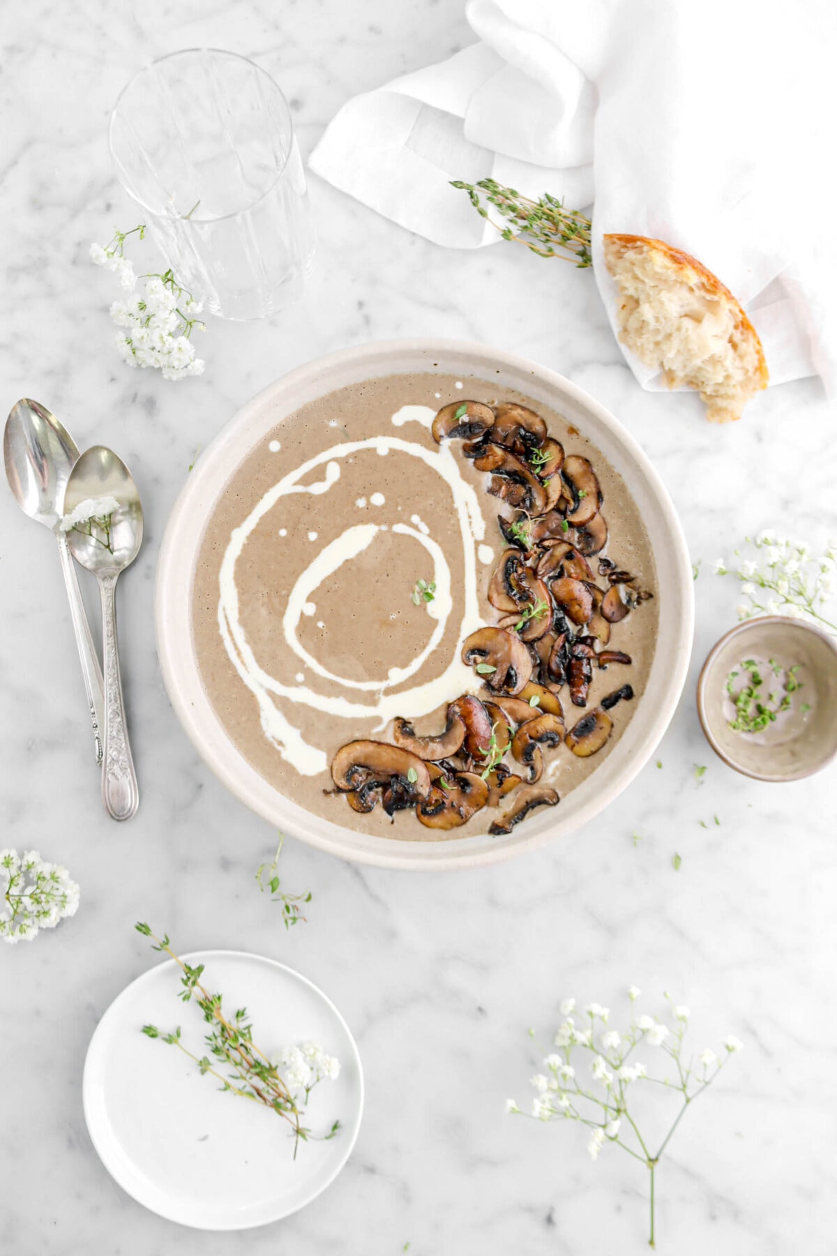 pulled back overhead shot of cream of mushroom soup in large bowl with plate of thyme sprigs, brown bowl, and two spoons beside.