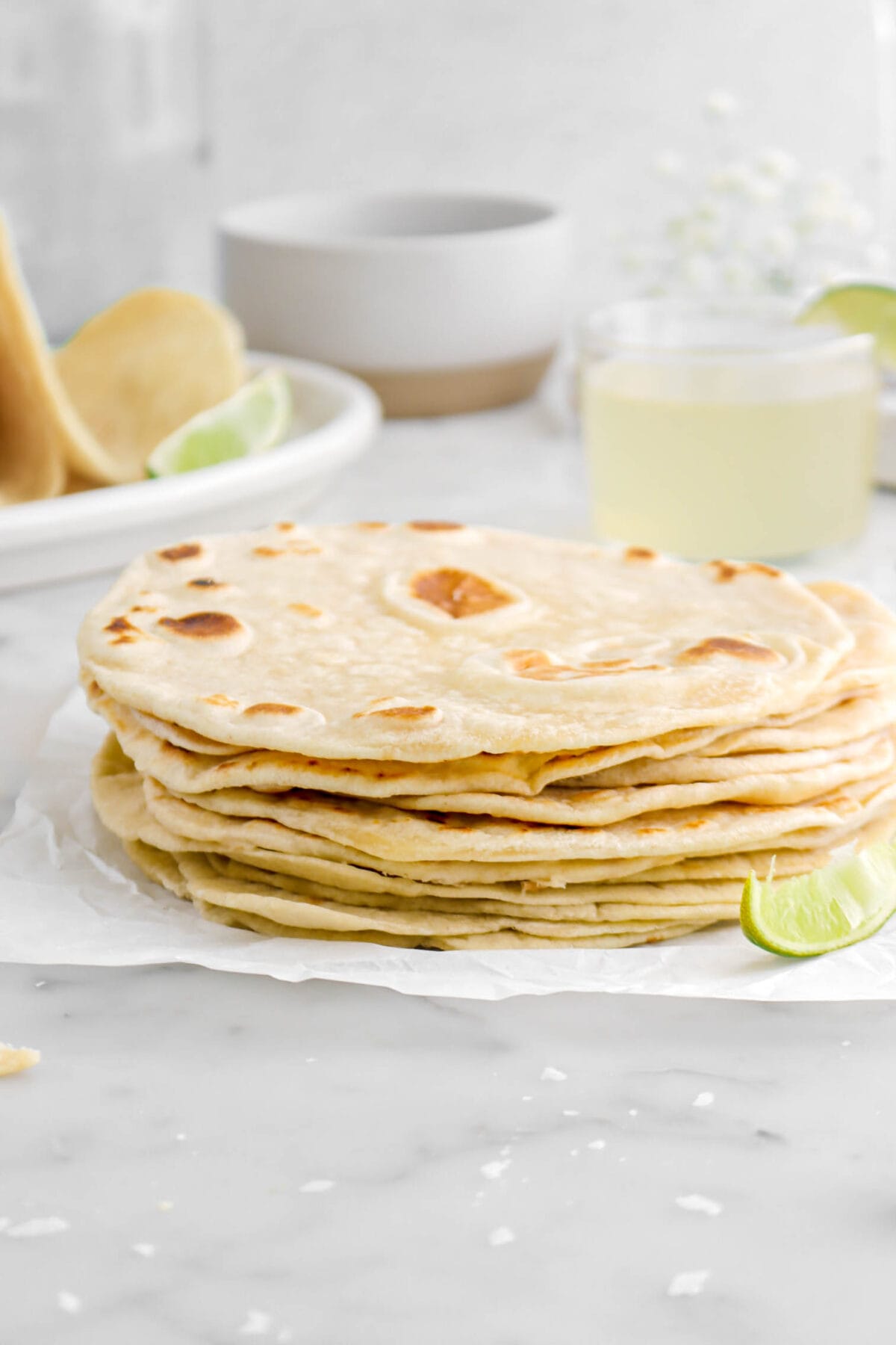 close up of stacked tortillas on parchment paper with bowl and margarita behind
