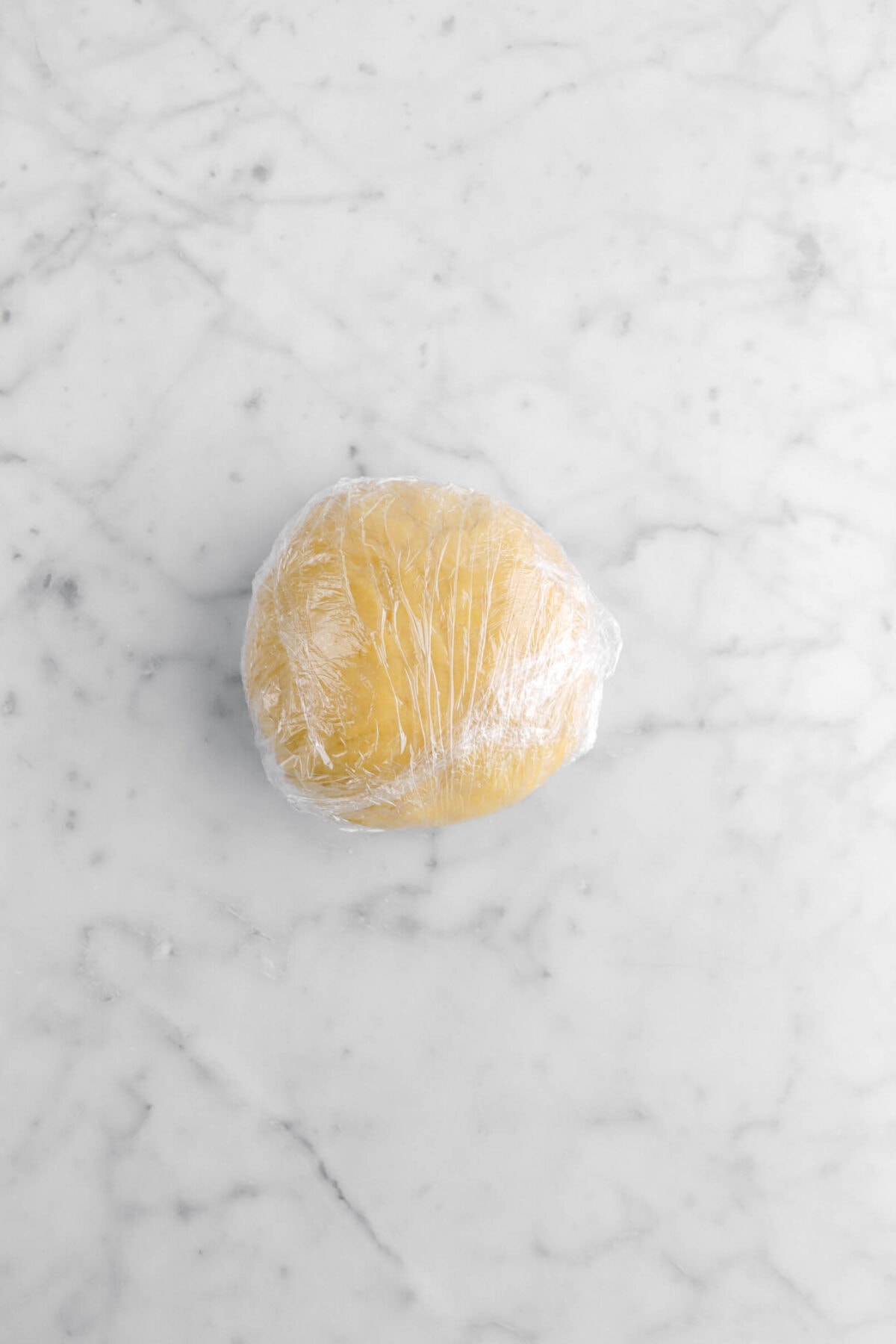 pasta dough wrapped in plastic wrap on marble surface.