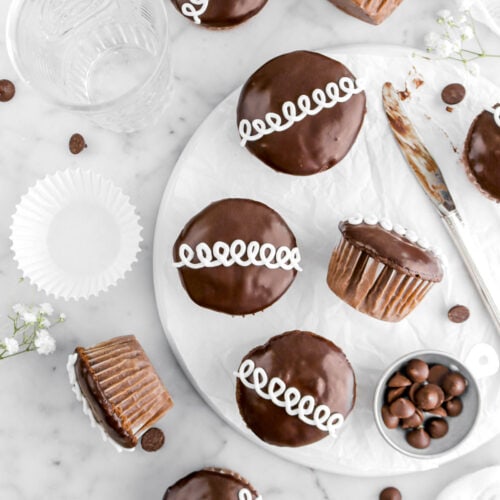 overhead shot of nine hostess cupcakes with three turned on their side, empty cupcake paper beside with white flowers and chocolate chip around on marble surface.