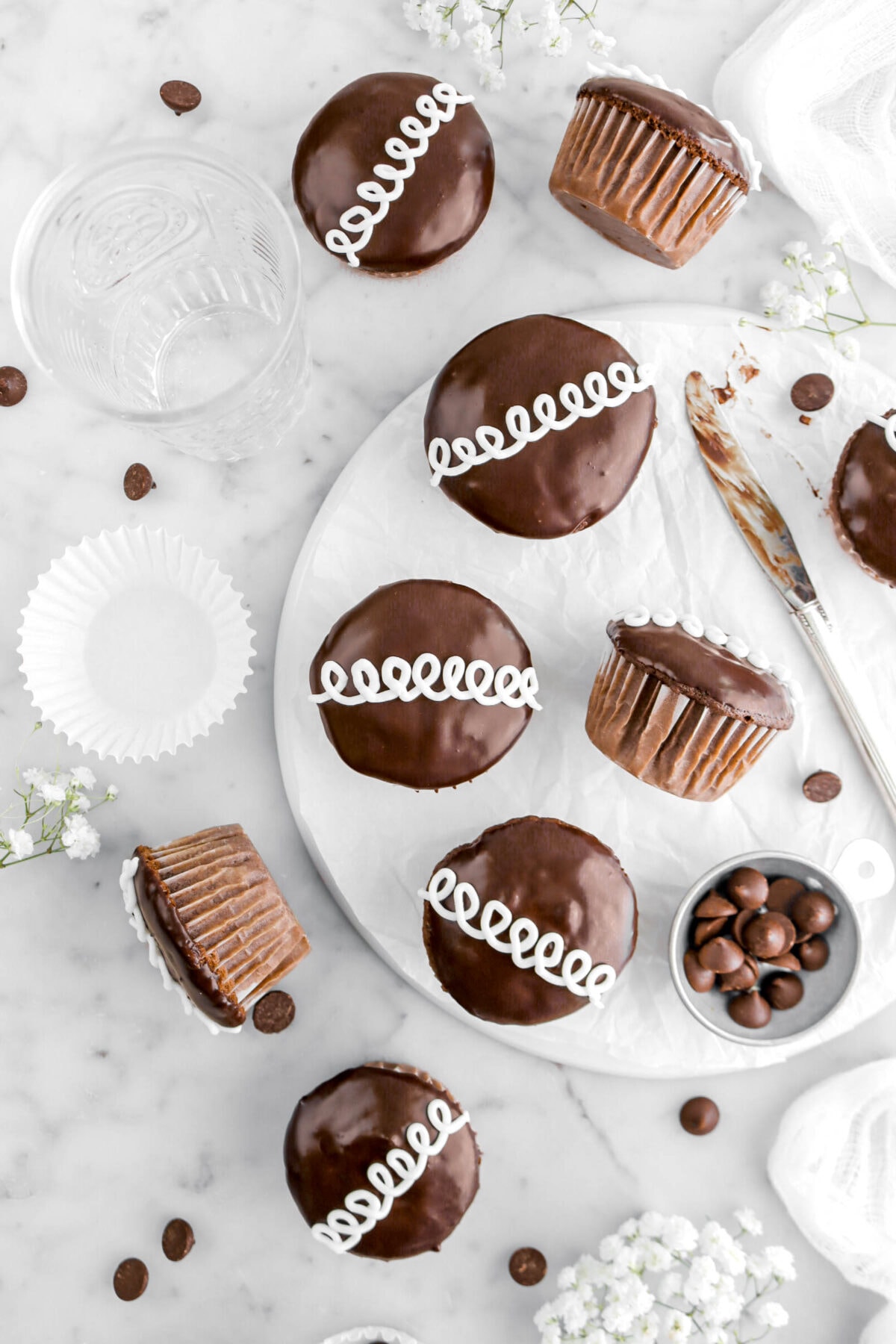 overhead shot of nine hostess cupcakes with three turned on their side, empty cupcake paper beside with white flowers and chocolate chip around on marble surface.