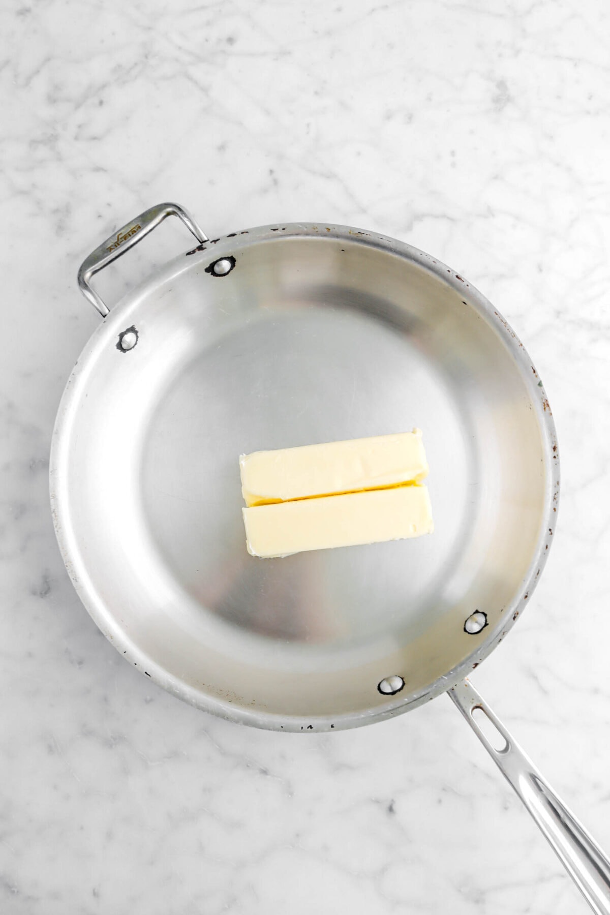 two sticks of butter in large skillet on marble surface.