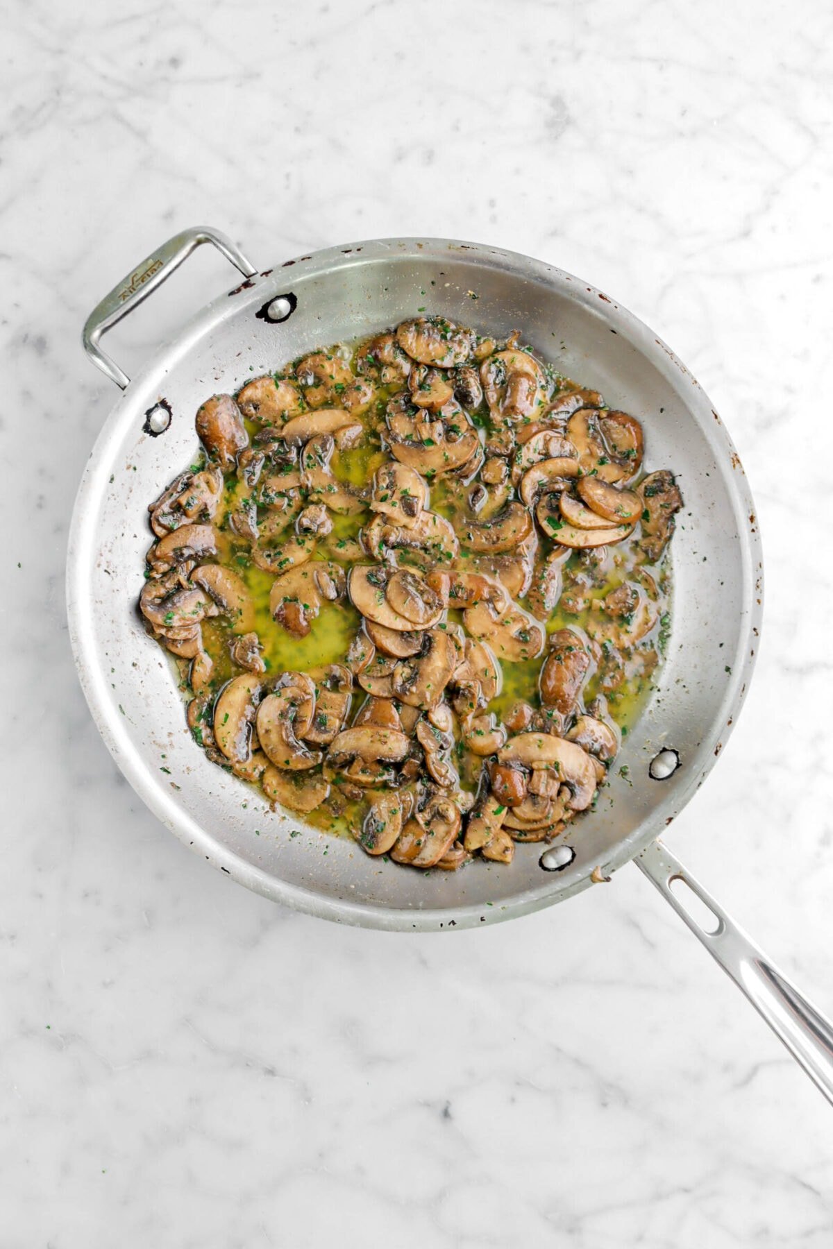 Sautéed mushrooms and herbs in skillet on marble surface.