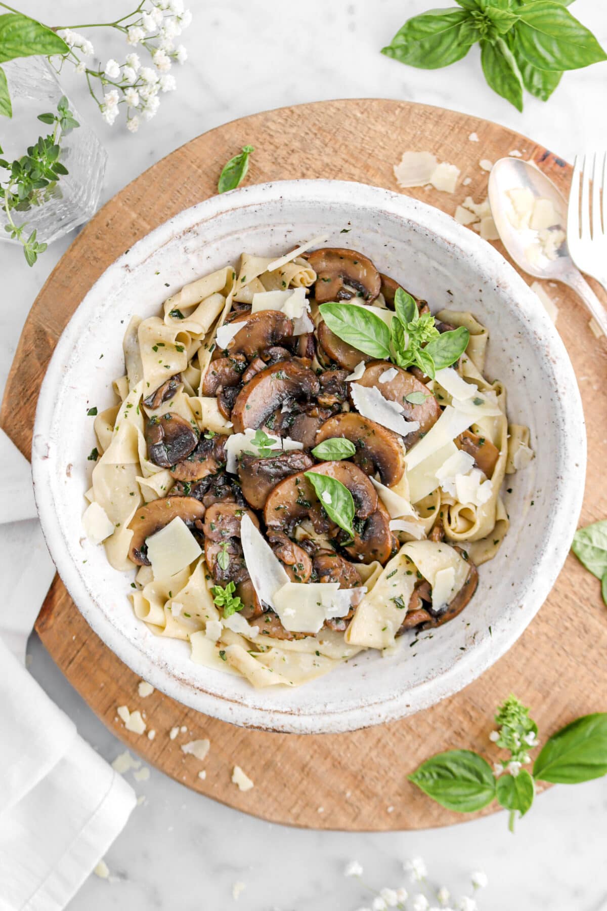 mushroom tagliatelle on wood board with basil and thyme around and grated cheese.